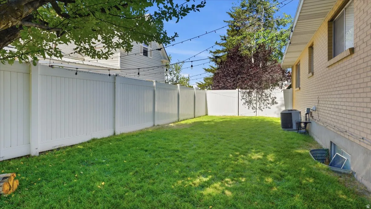 Expansive backyard featuring a manicured lawn, a full-height white privacy fence, and a brick exterior with multiple windows