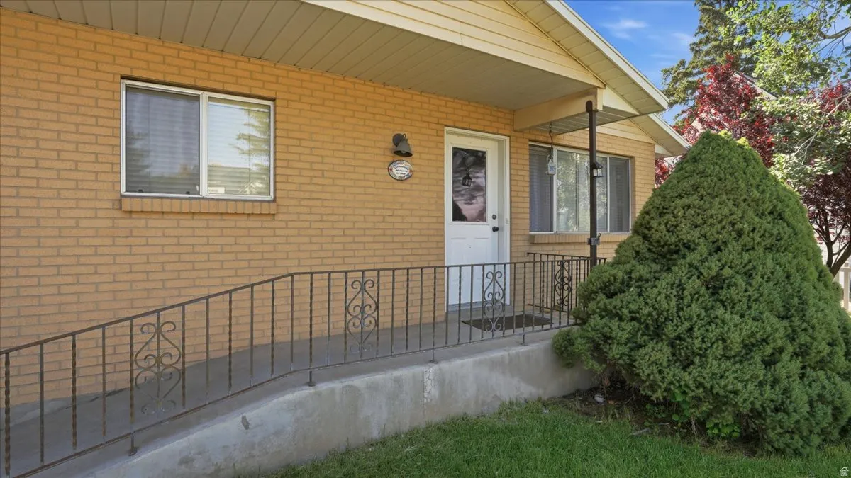 Brick exterior featuring a covered entry, white paneled door, decorative wrought iron railing, and a concrete ramp