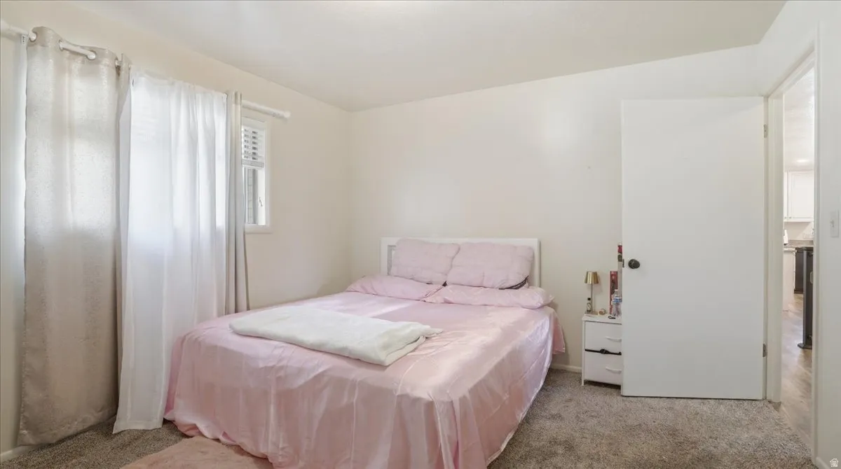 Bedroom featuring light-toned walls, a window with horizontal blinds, and neutral-toned carpeting