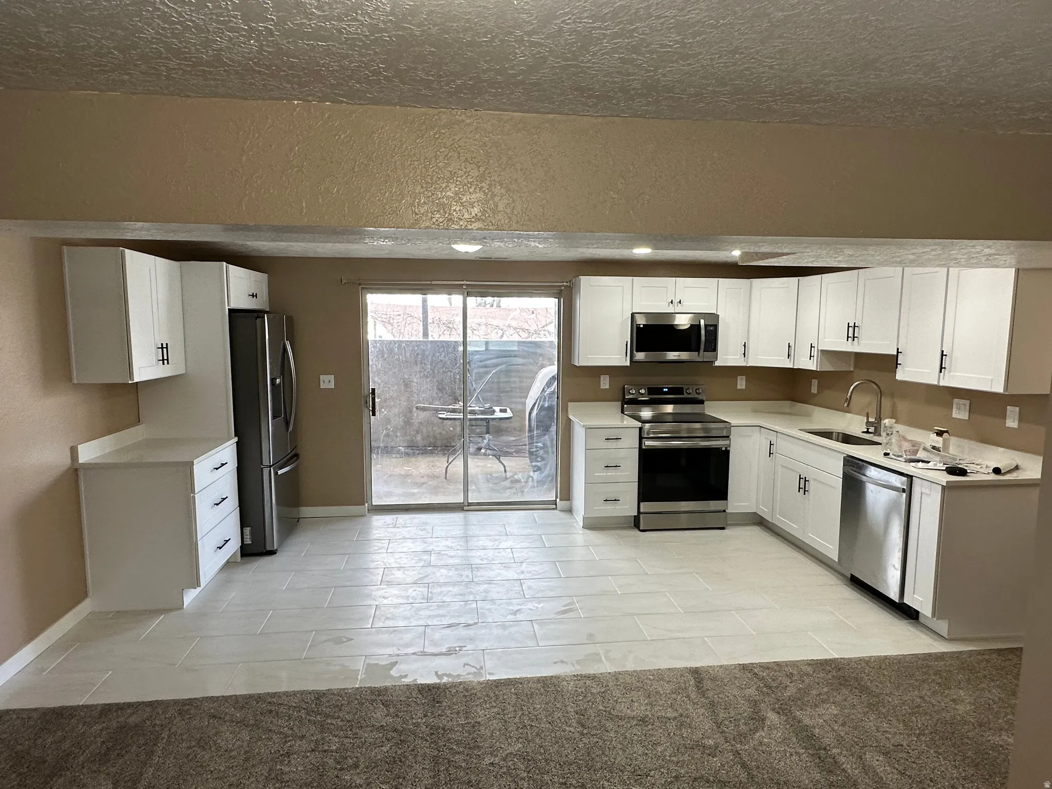 Modern kitchen featuring white shaker cabinetry, stainless steel appliances, light-toned countertops, and light-colored tile flooring