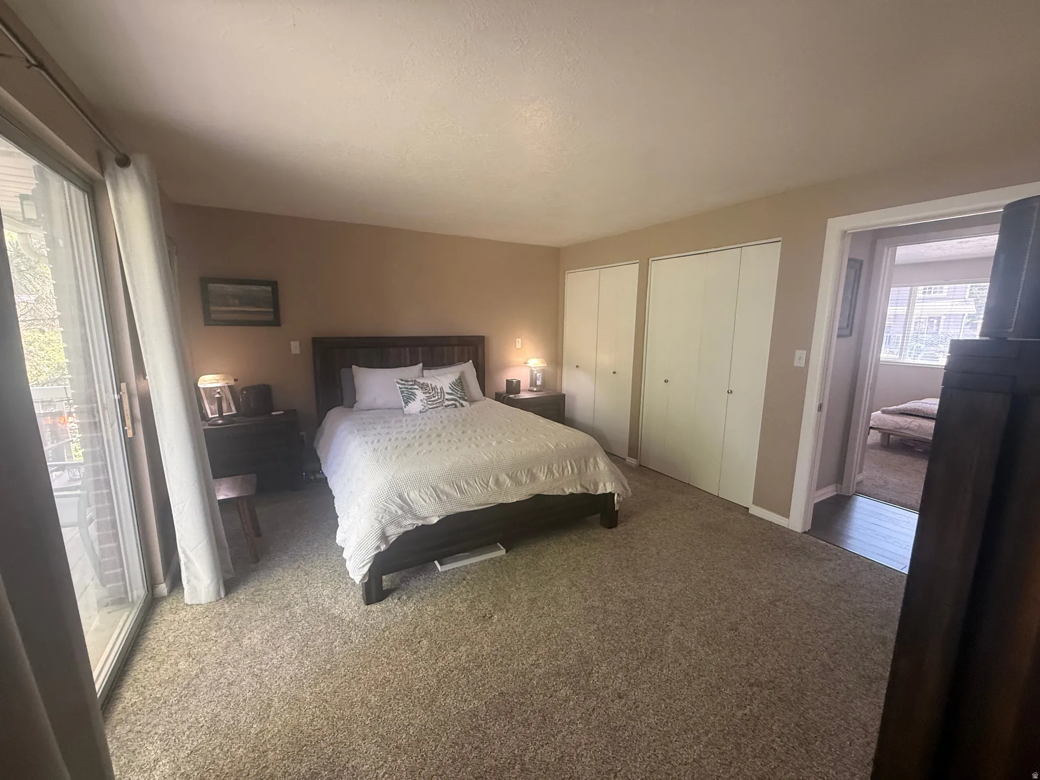 Plush carpeting throughout, featuring two bi-fold door closets, and a glass sliding door providing outdoor access