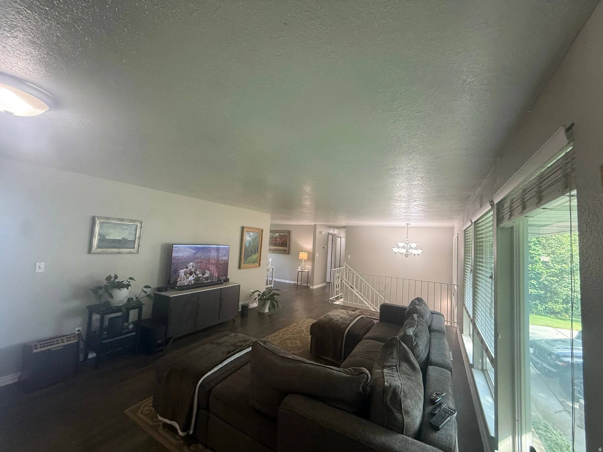 Spacious living area featuring wood-finish flooring, ample natural light from large windows, and a dedicated dining space with a chandelier