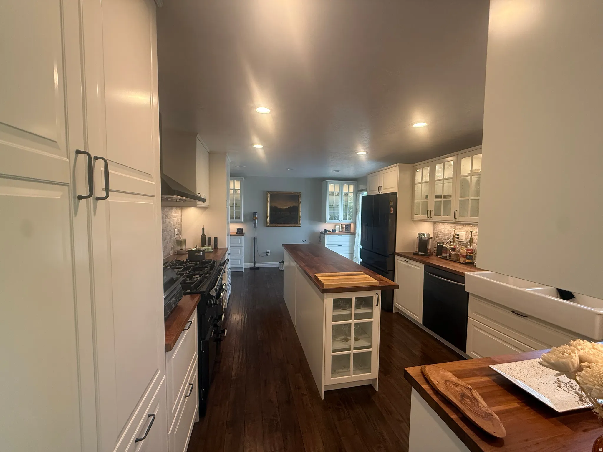 Bright kitchen featuring white shaker cabinetry, dark wood-finish flooring, butcher block countertops, a center island with built-in storage, and integrated appliances