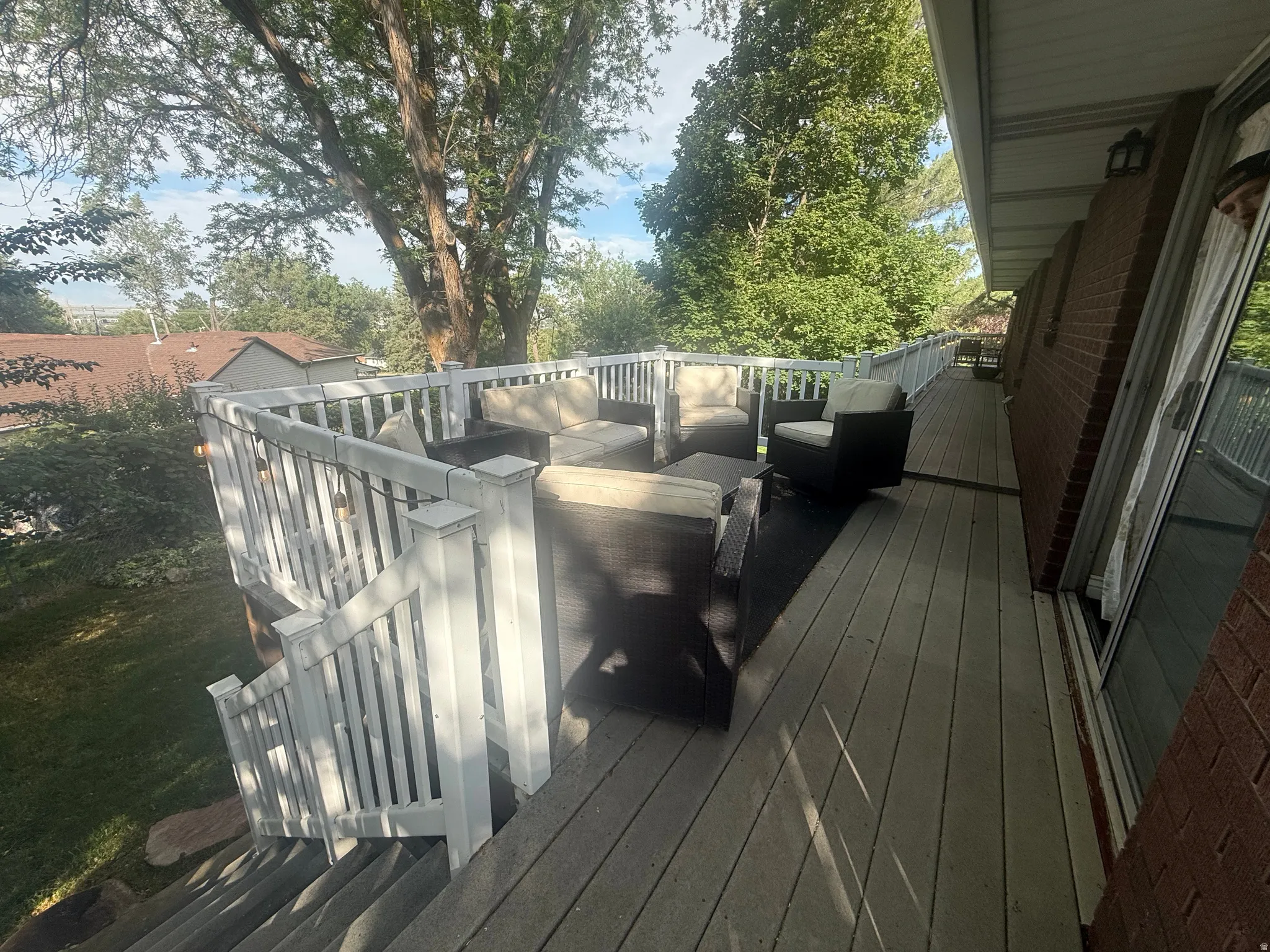Expansive outdoor deck featuring wood-finish flooring, white railings, and direct access to interior spaces through a sliding glass door