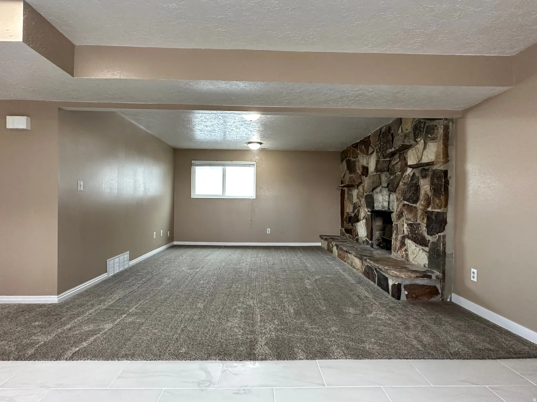 Spacious room featuring a stone fireplace with hearth, plush carpet flooring, a large window, and recessed lighting