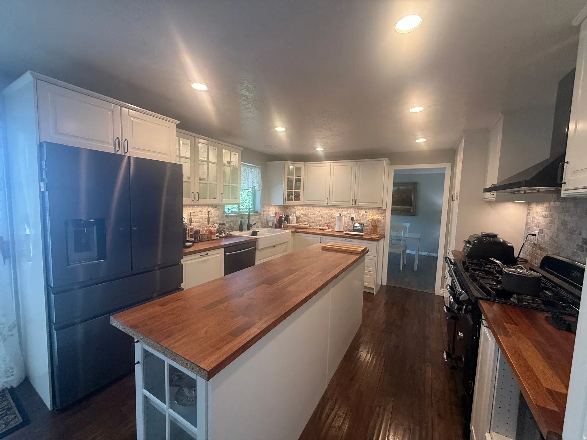Spacious kitchen featuring an island with a wood-finish countertop, stainless steel refrigerator, white cabinetry, dark wood-finish flooring, and recessed lighting