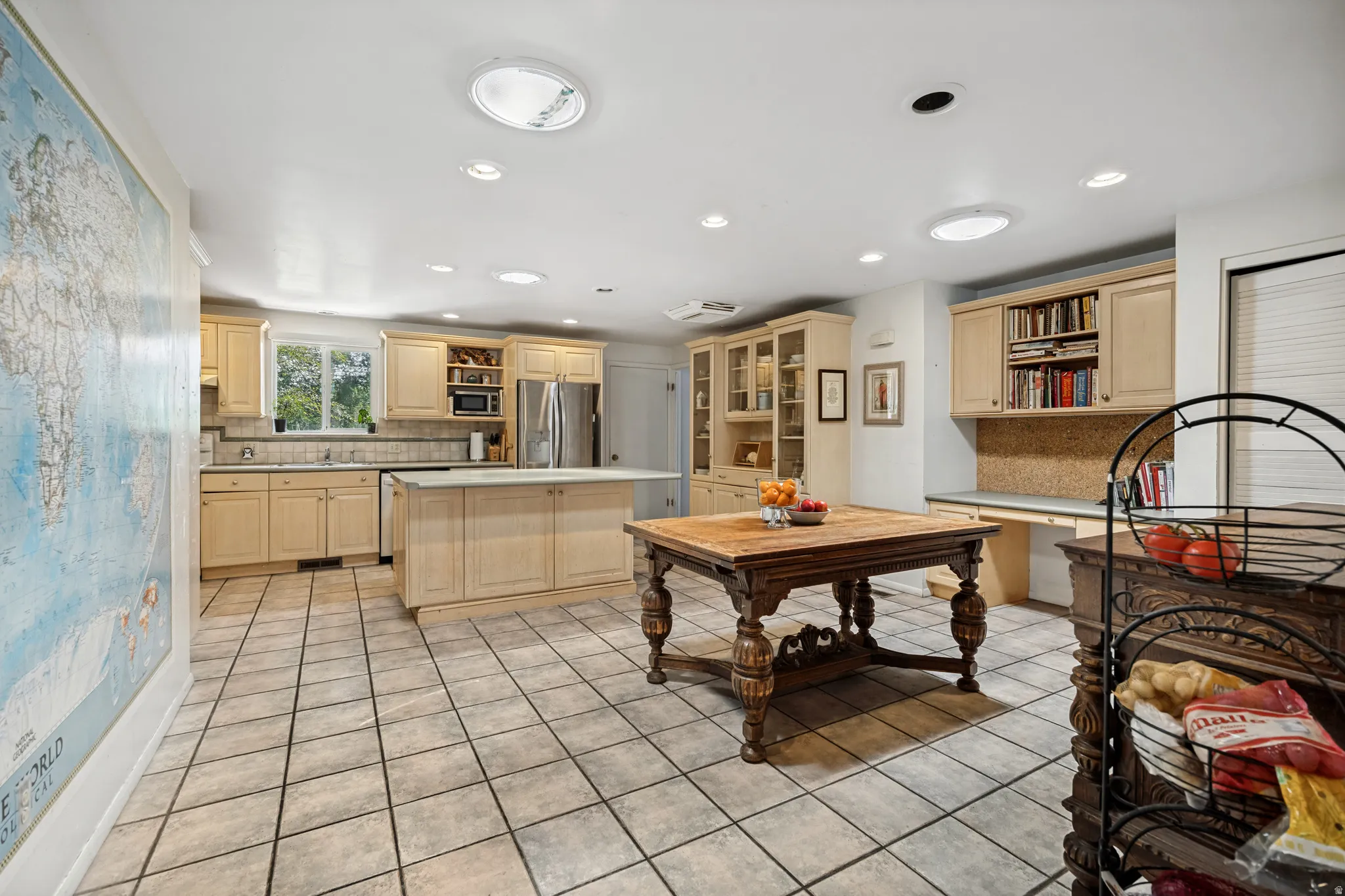 Spacious kitchen featuring tile flooring, light wood cabinetry, a central island, stainless steel appliances, and multiple recessed light fixtures