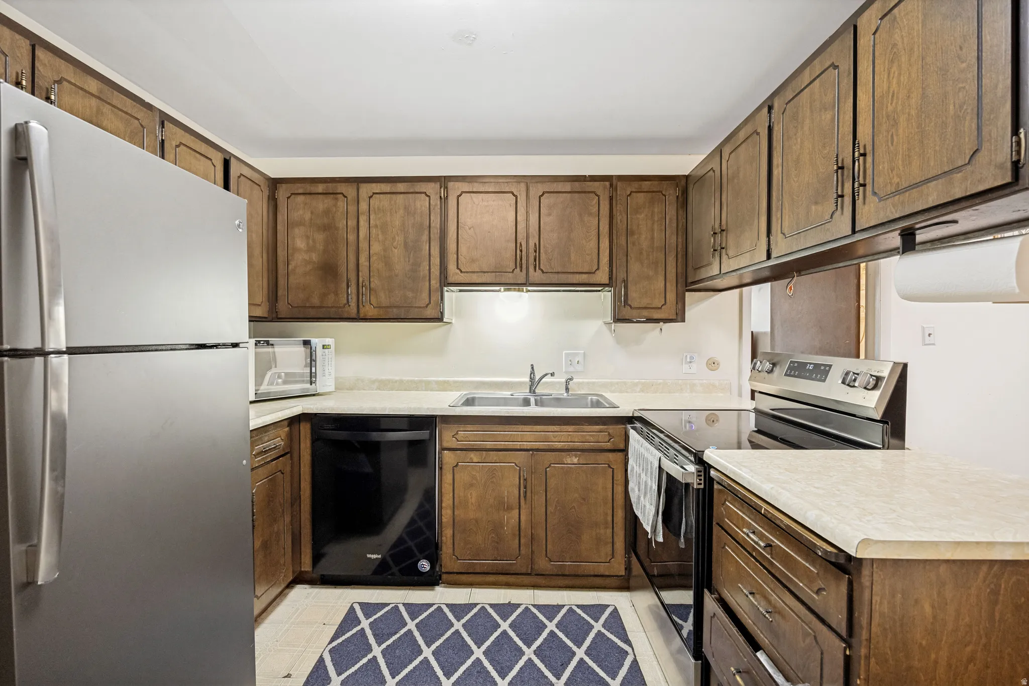 Functional kitchen featuring wood cabinetry, light-toned countertops, a stainless steel refrigerator, and a stainless steel range with a flat cooktop