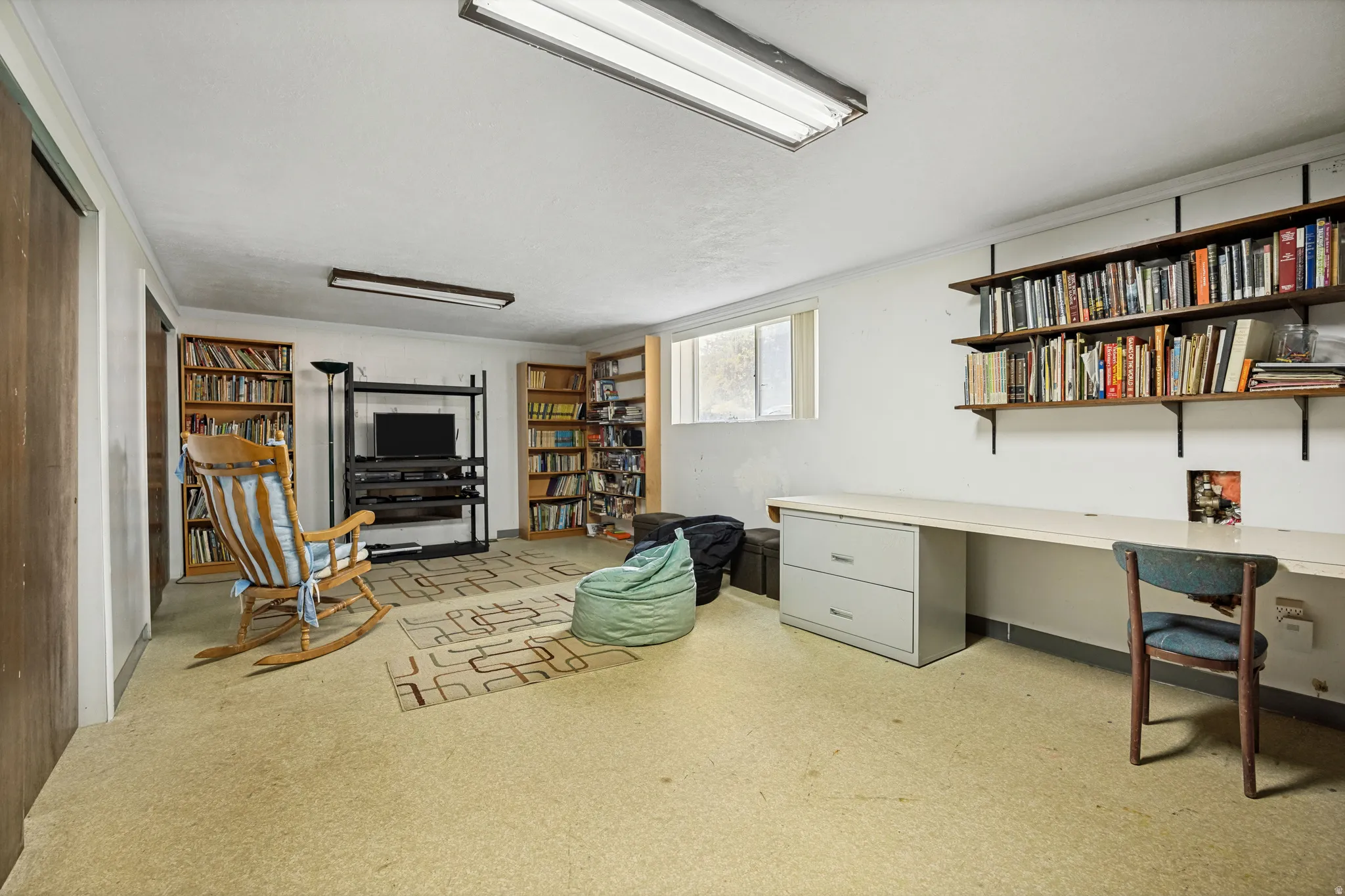 Spacious room featuring light-colored carpeting, a built-in wall desk with a filing cabinet, and integrated shelving