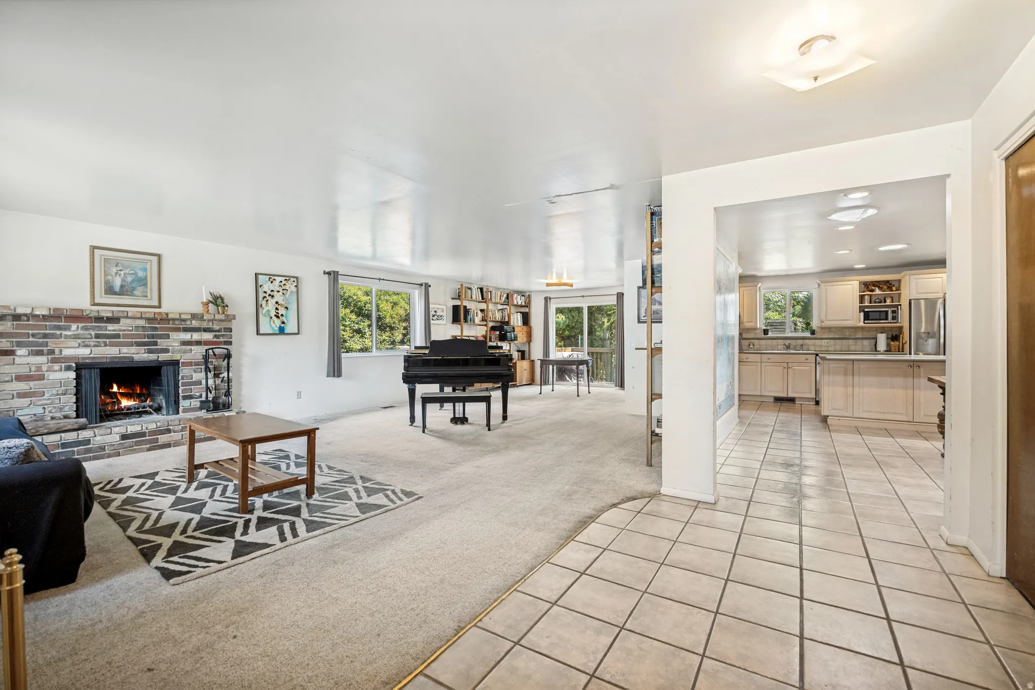 Spacious living area featuring a brick-surround fireplace, light-colored carpeting, multiple windows for natural light, and recessed lighting