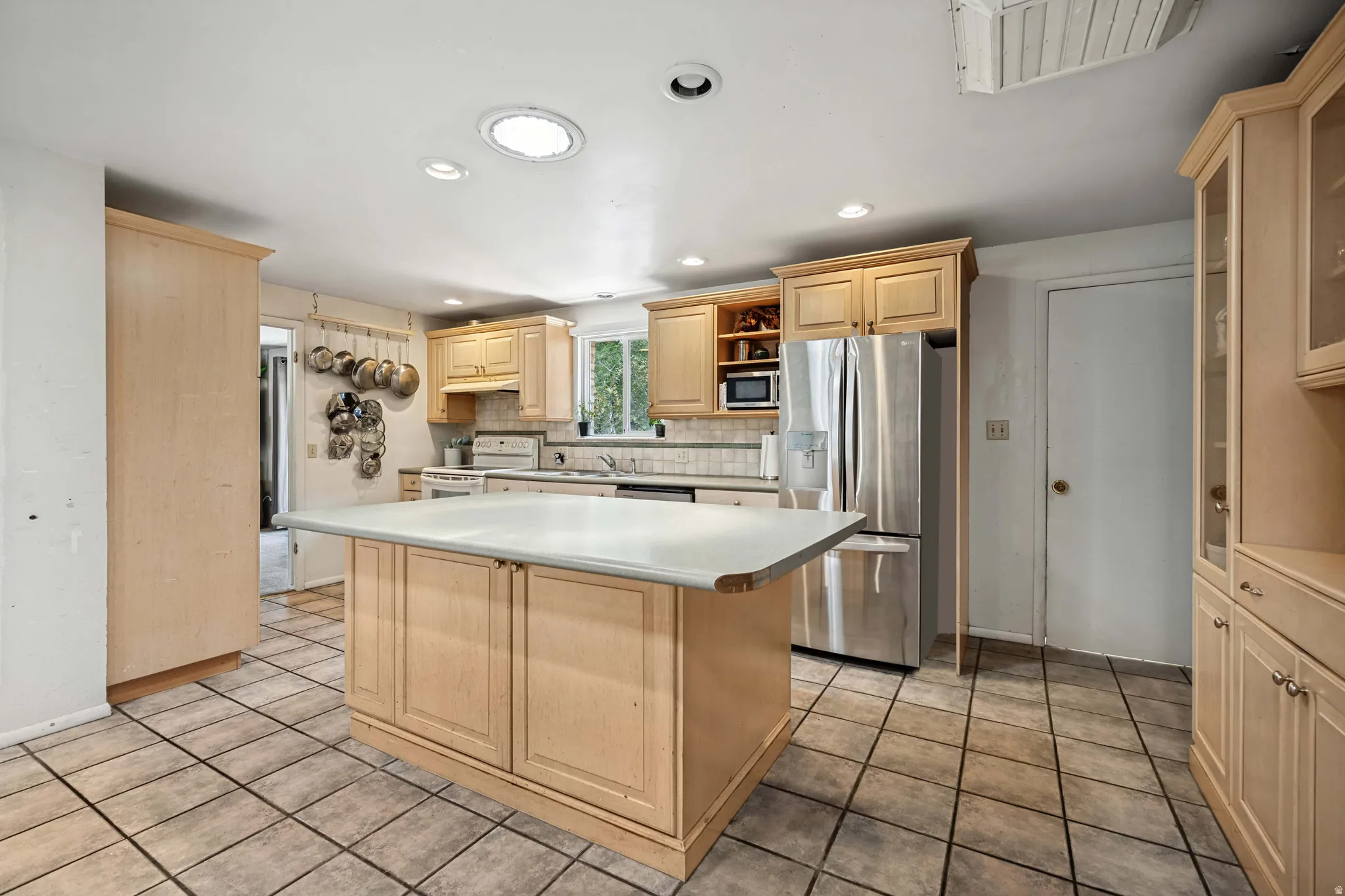 Kitchen featuring a central island with countertop, light wood-finish cabinetry, tile flooring, recessed lighting, and a stainless steel refrigerator