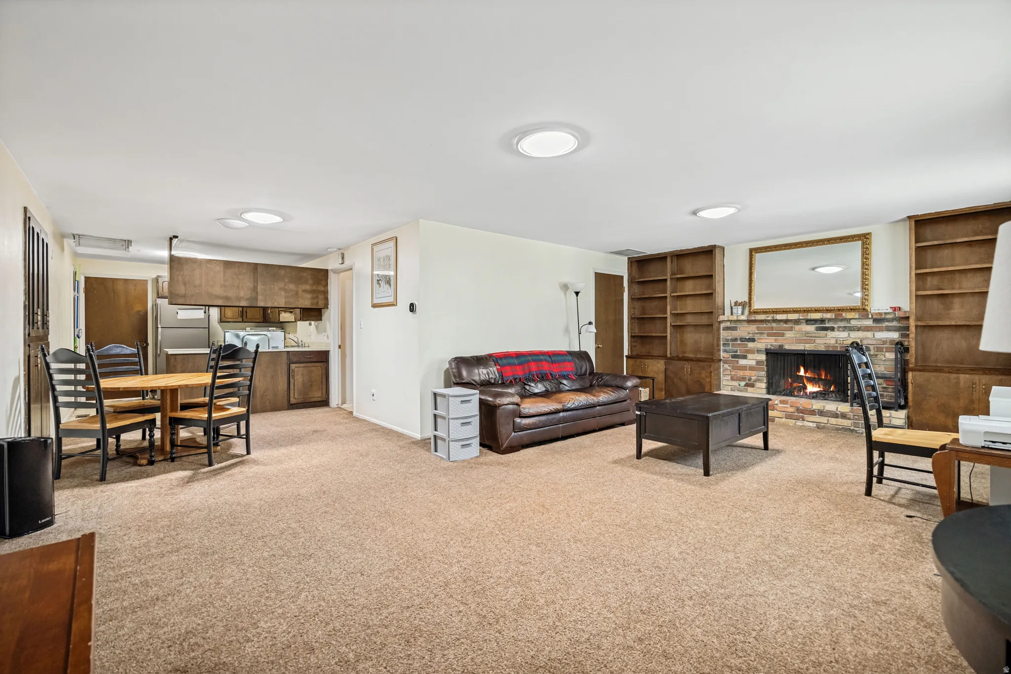 Open concept living space featuring a brick fireplace with a wood mantel, built-in shelving, recessed lighting, and wood-finish cabinetry