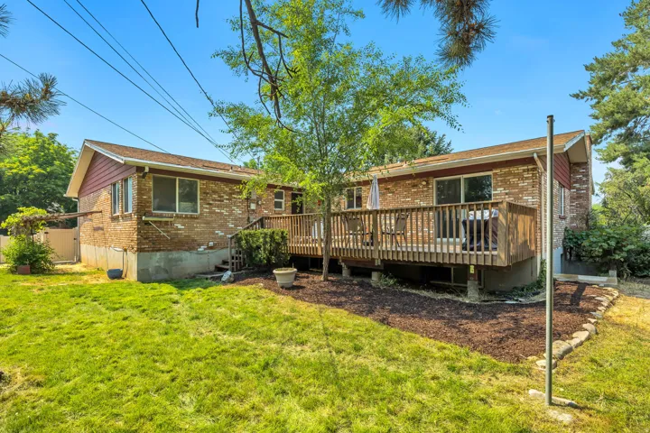 Brick exterior with red siding accents, featuring a spacious wood deck, a manicured lawn, mature trees, and a decorative rock border
