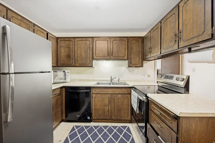 Functional kitchen featuring wood cabinetry, light-toned countertops, a stainless steel refrigerator, and a stainless steel range with a flat cooktop