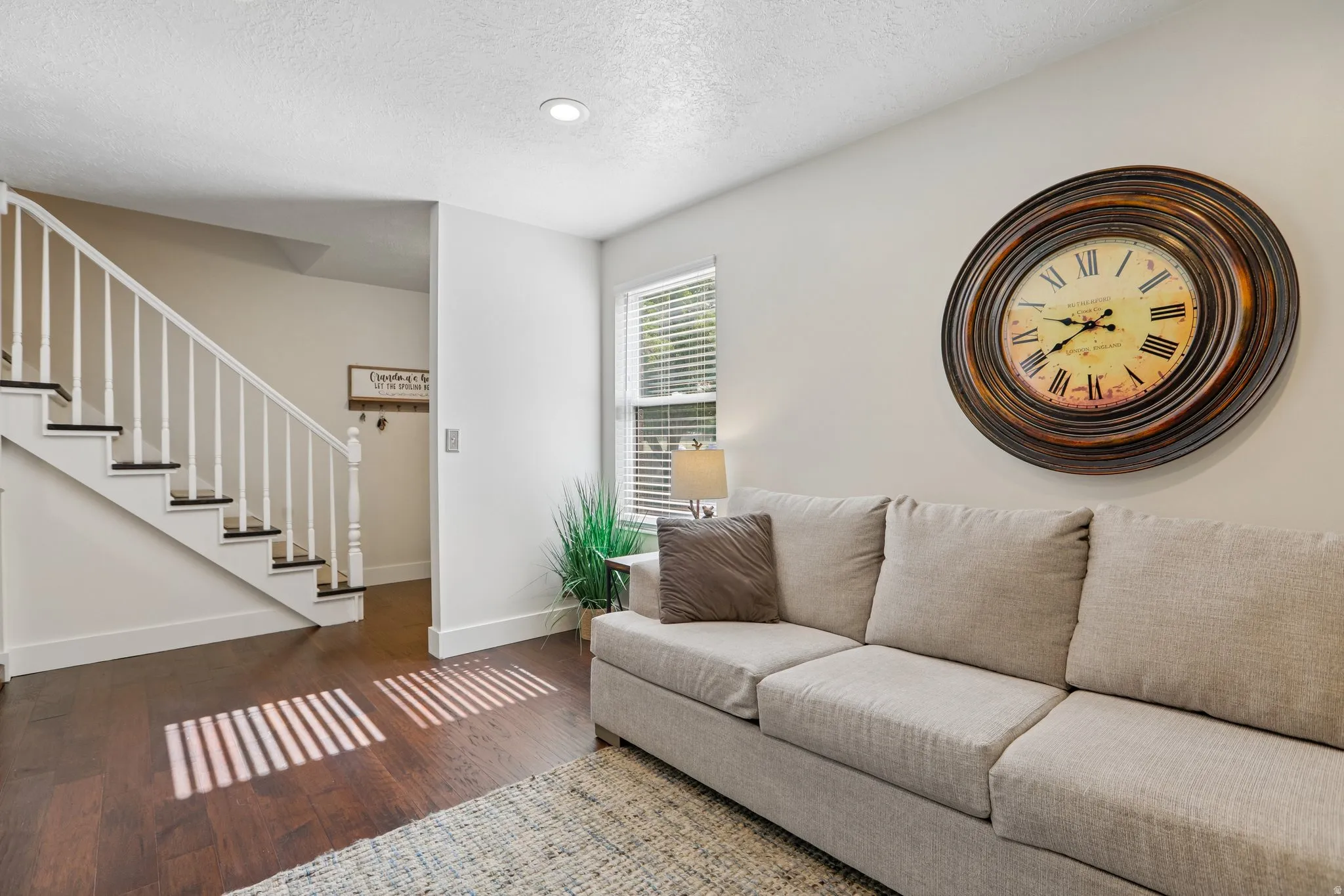 Living area featuring dark wood-finish flooring, white baseboards, and a bright window with blinds