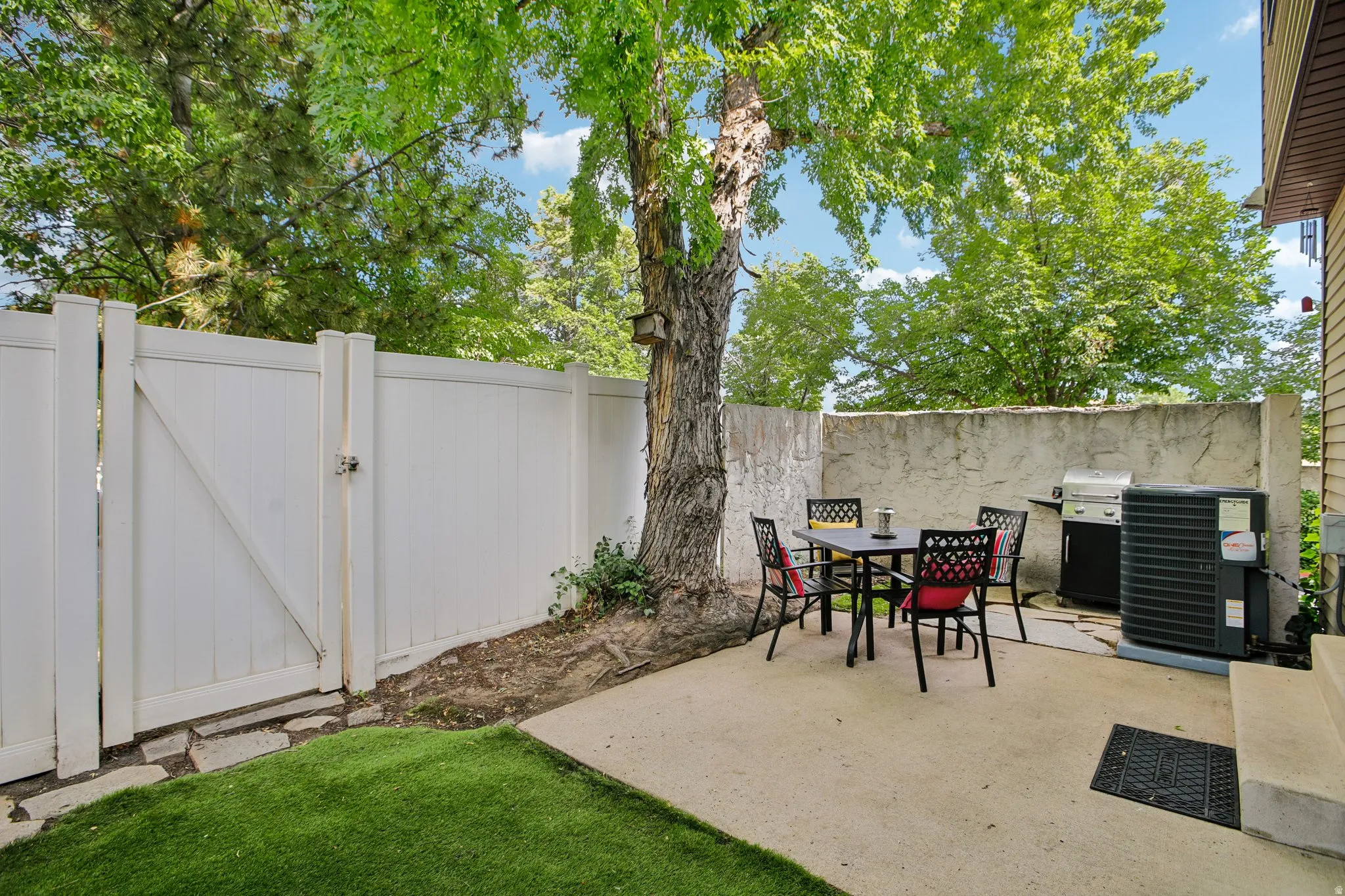 Private patio area featuring a concrete surface, a partial privacy wall, and mature tree