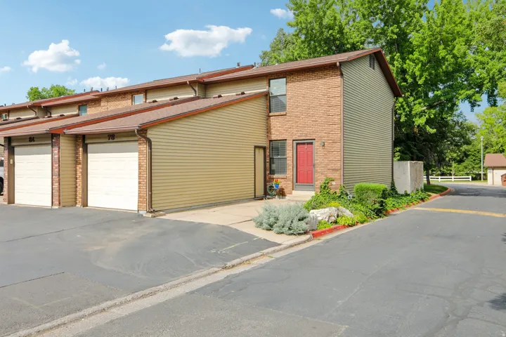Townhome exterior featuring tan siding, brick accents, a red entry door, and an attached garage with a paved driveway