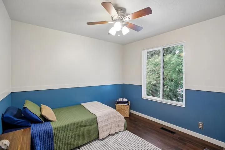 Bedroom featuring wood-finish flooring, a white-framed window with blinds, and a ceiling fan with integrated lighting