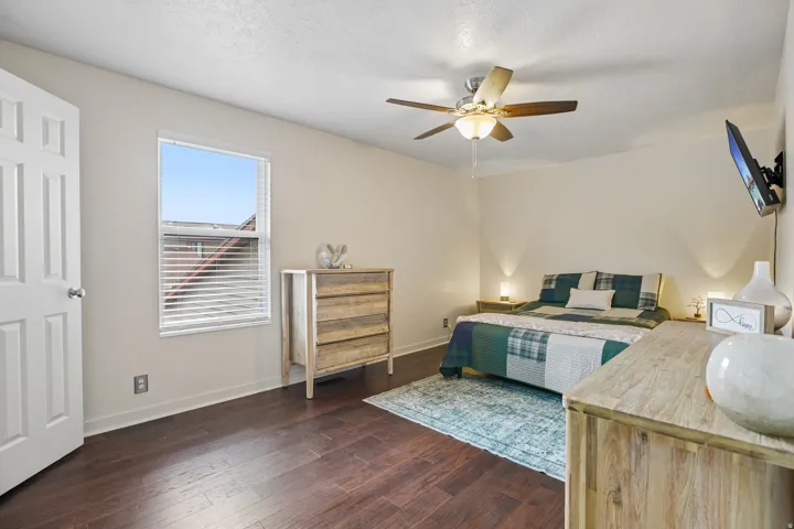 Spacious bedroom featuring wood-finish flooring, a ceiling fan, and a large window with blinds