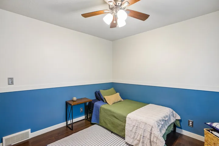 Room featuring wood-finish flooring, two-tone wall treatment, and a ceiling fan with integrated lighting