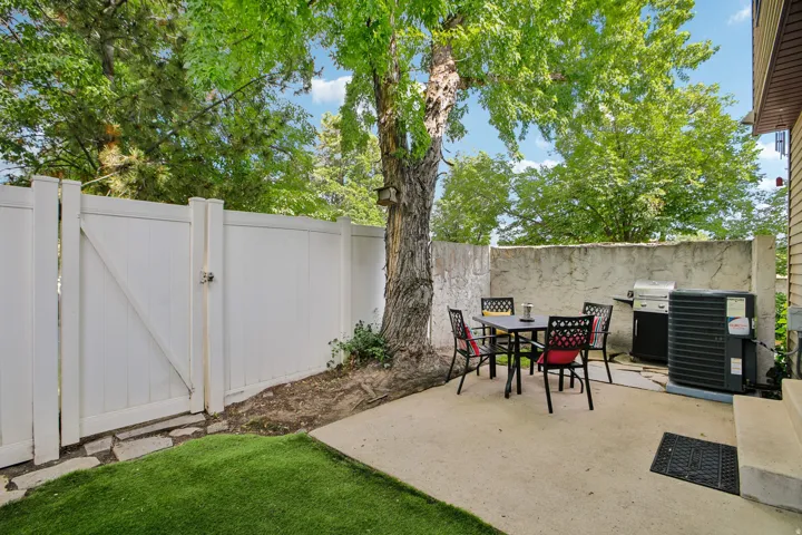 Private patio area featuring a concrete surface, a partial privacy wall, and mature tree