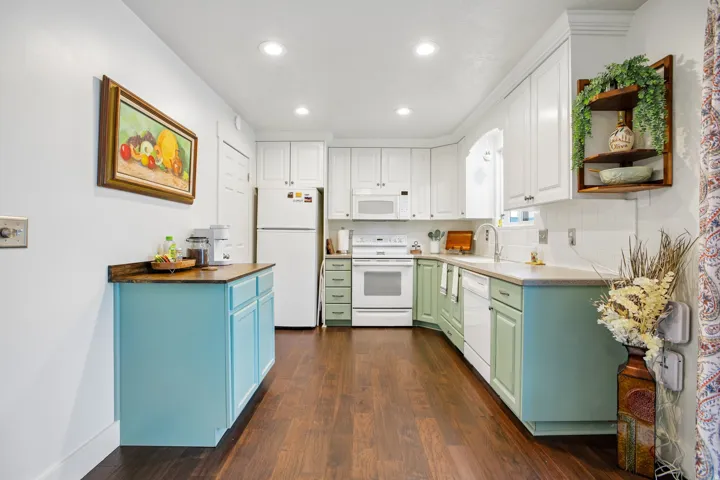 Kitchen featuring a combination of white and colored cabinetry, wood-finish flooring, white appliances, recessed lighting, and a white tile backsplash