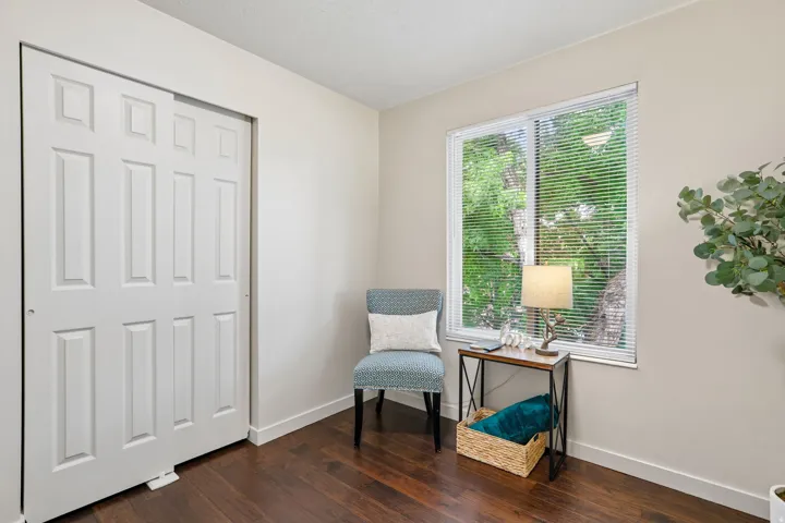 Bright room featuring rich wood-finish flooring, light-colored walls, and a window with horizontal blinds