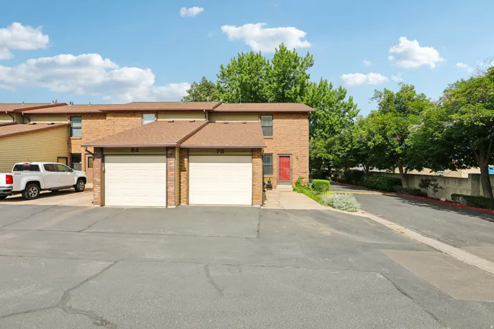 Brick exterior townhome featuring a private attached garage, individual red entry door, and gabled roofline