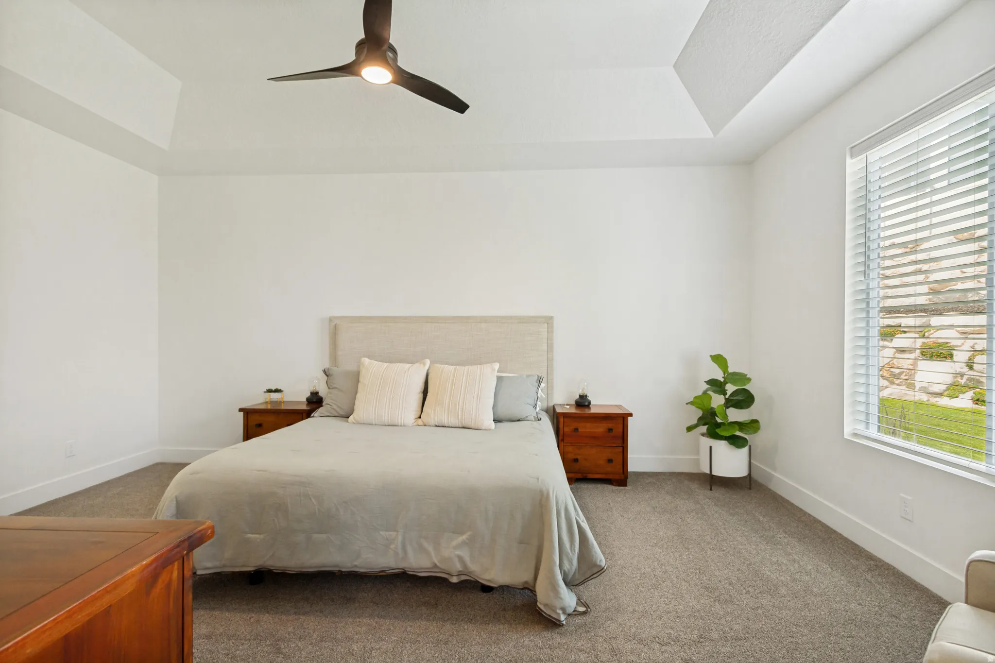 Spacious room featuring a tray ceiling with a contemporary ceiling fan, large window with blinds, and neutral-toned carpeting
