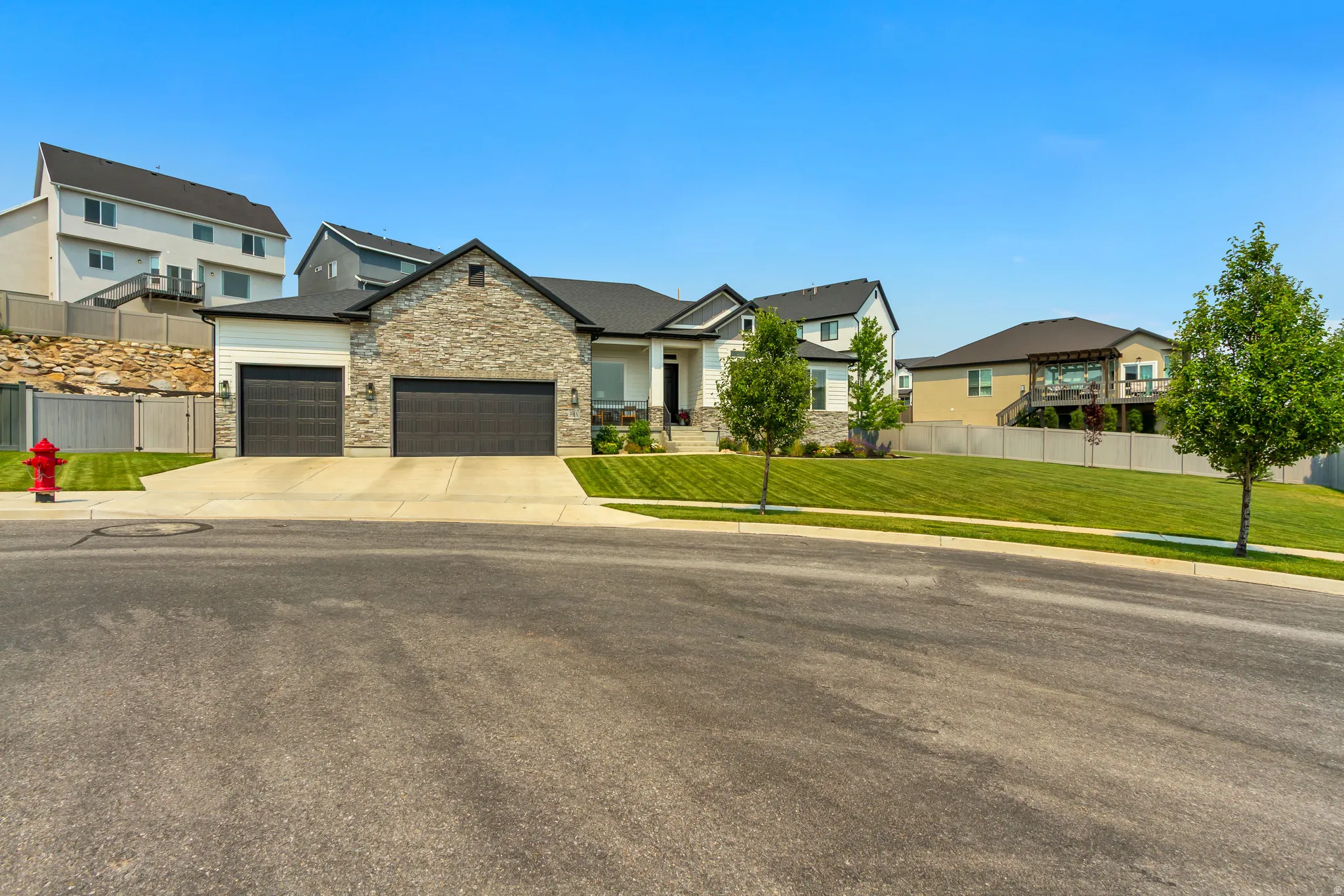Contemporary residence featuring a stone and siding facade, a two-car garage with dark paneled doors, and a well-maintained front lawn