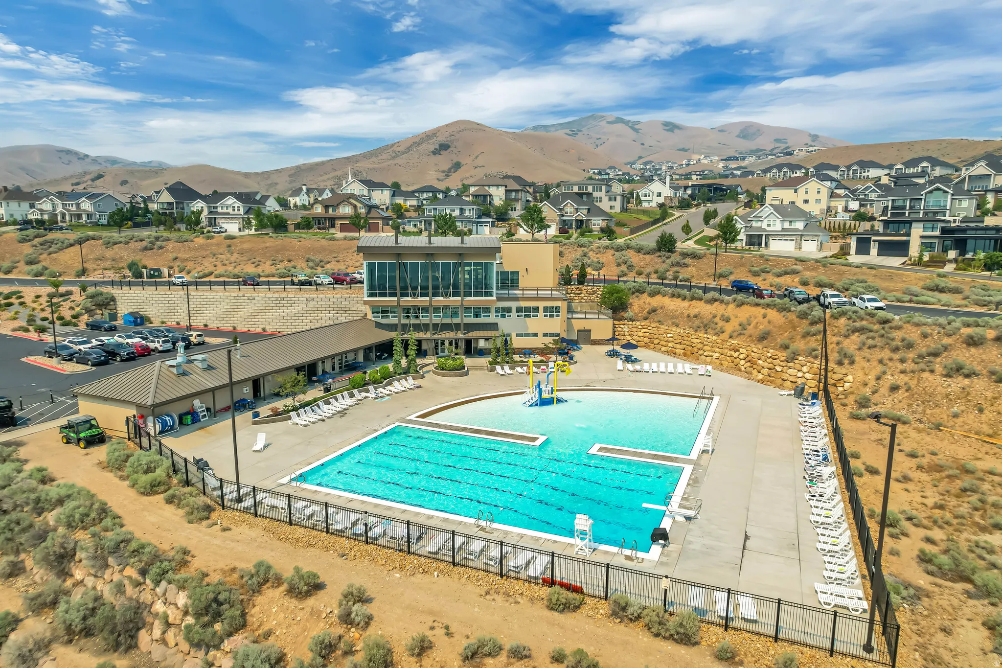 Expansive outdoor swimming pool area featuring multiple pools, surrounding hardscaping, and a substantial community building