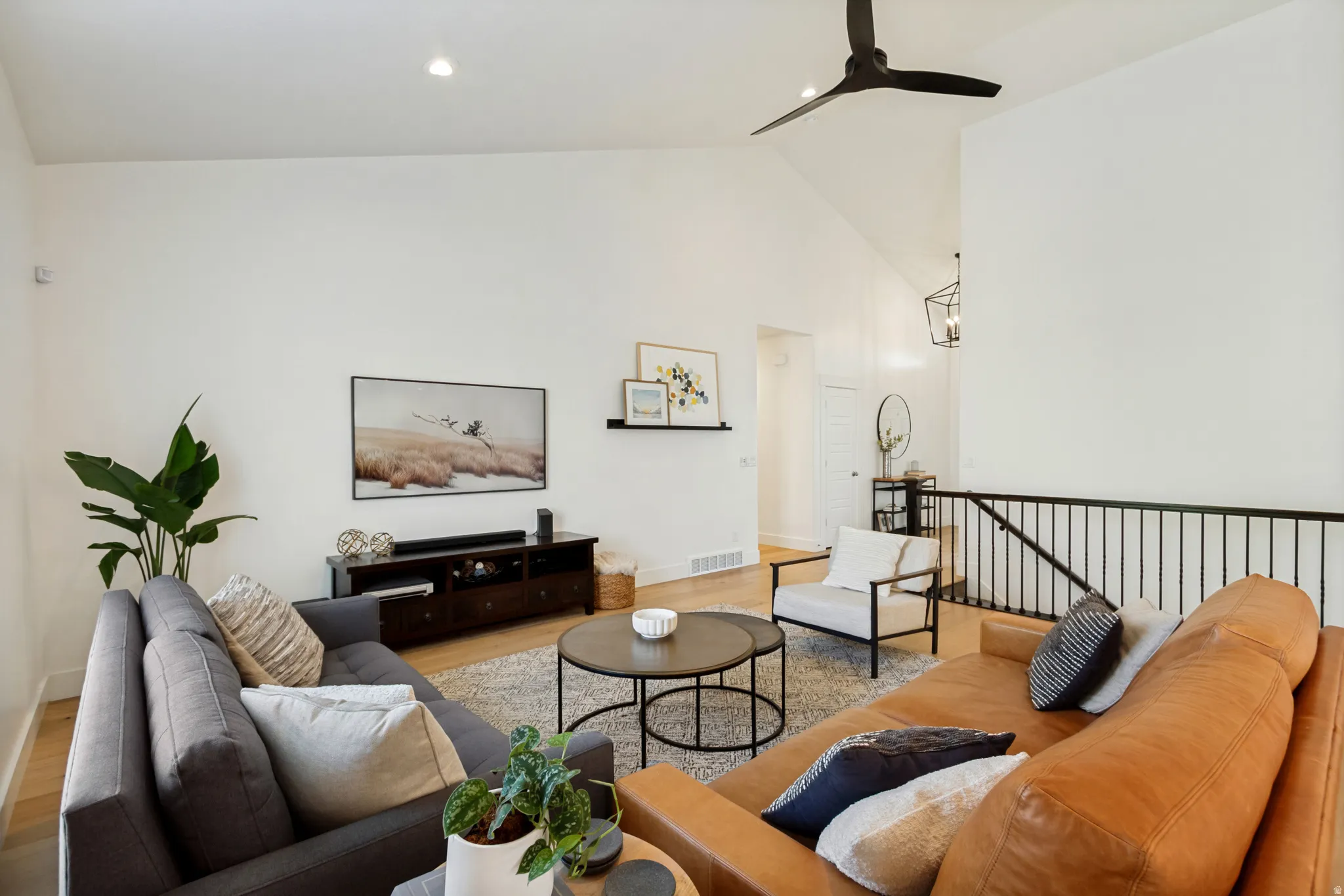 Spacious living area featuring vaulted ceilings, recessed lighting, wood-finish flooring, a contemporary ceiling fan, and a black metal railing