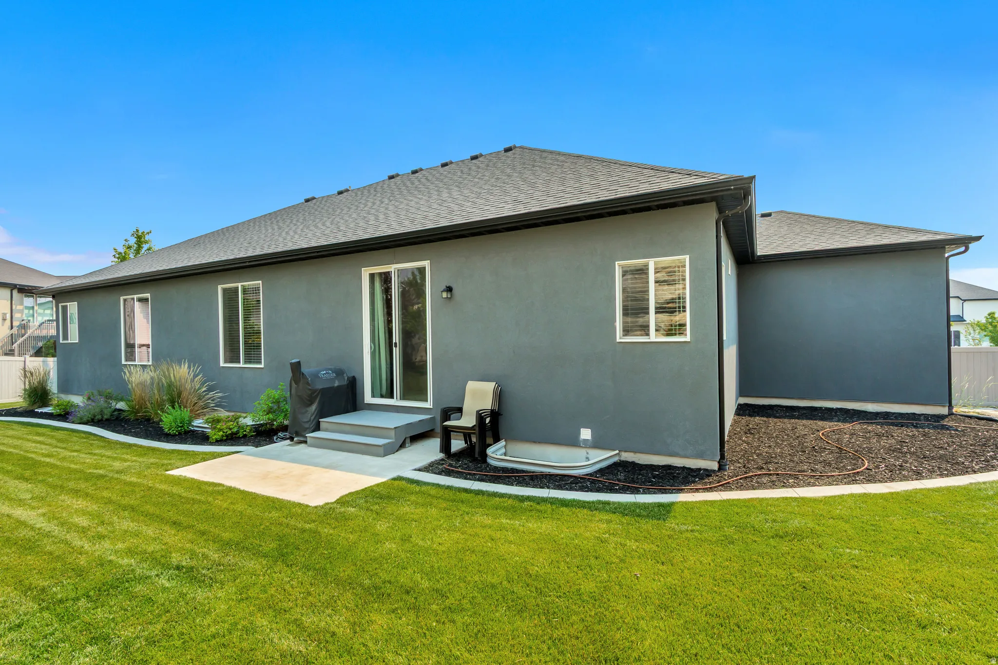 Expansive backyard featuring a manicured lawn, concrete patio, and landscaped beds with mature shrubs