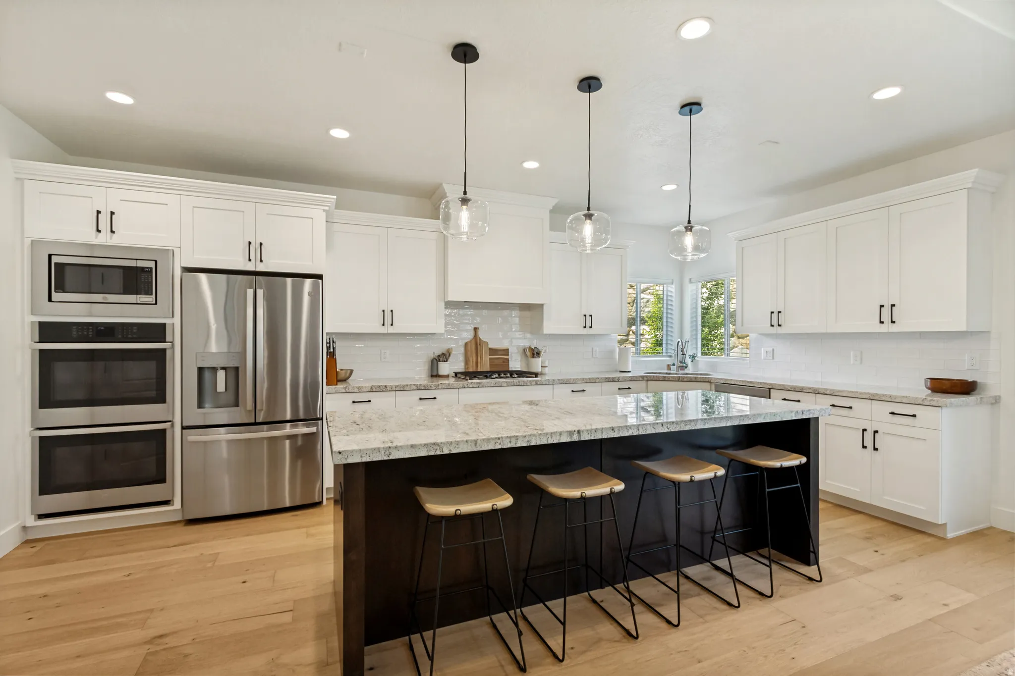 Modern kitchen featuring a dark-toned island with seating, light-toned wood-finish flooring, white cabinetry with dark hardware, stainless steel appliances, and light-toned countertops