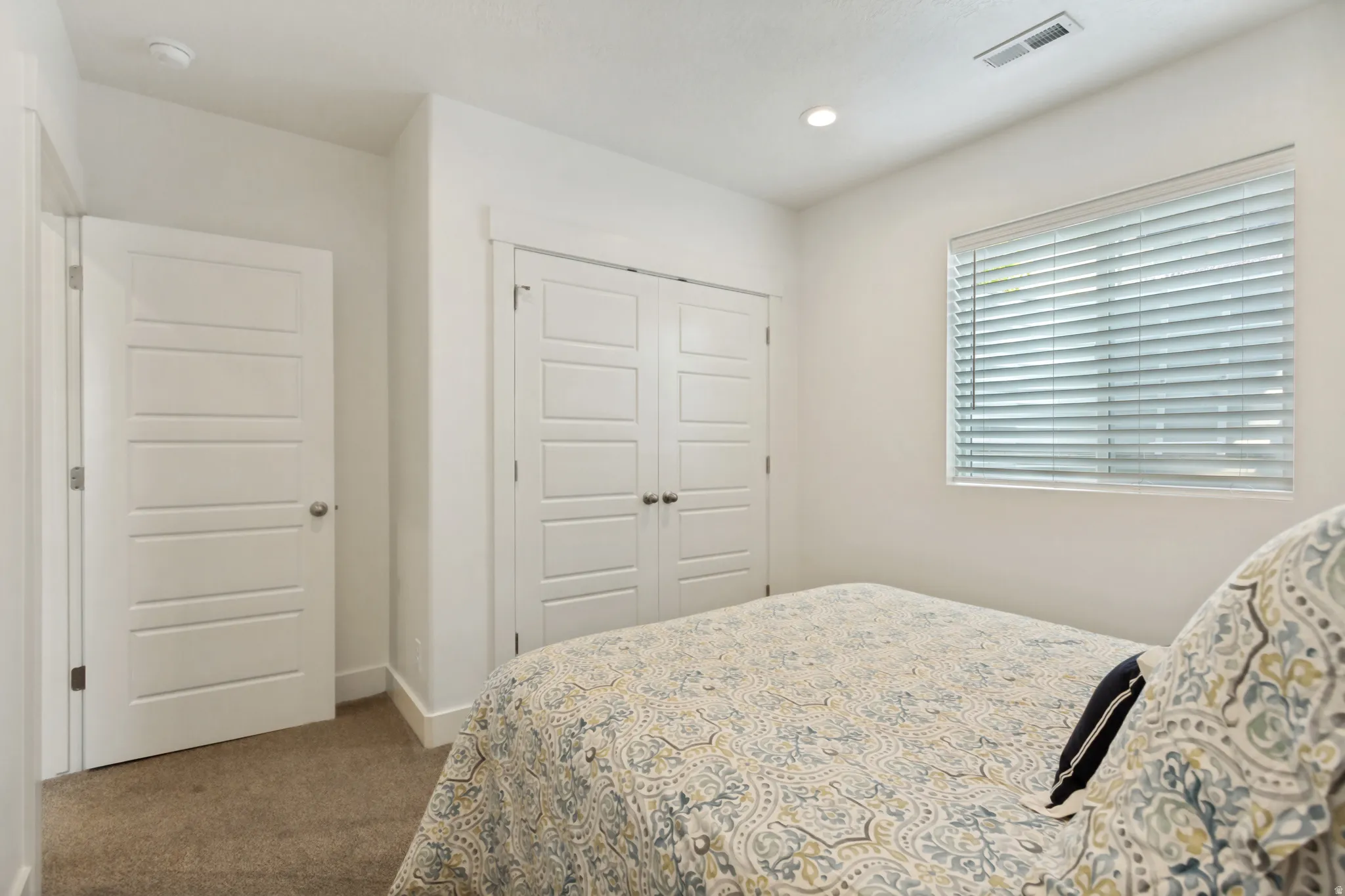 Carpeted room featuring a window with horizontal blinds, recessed ceiling lighting, and a bi-fold closet door with panel detailing