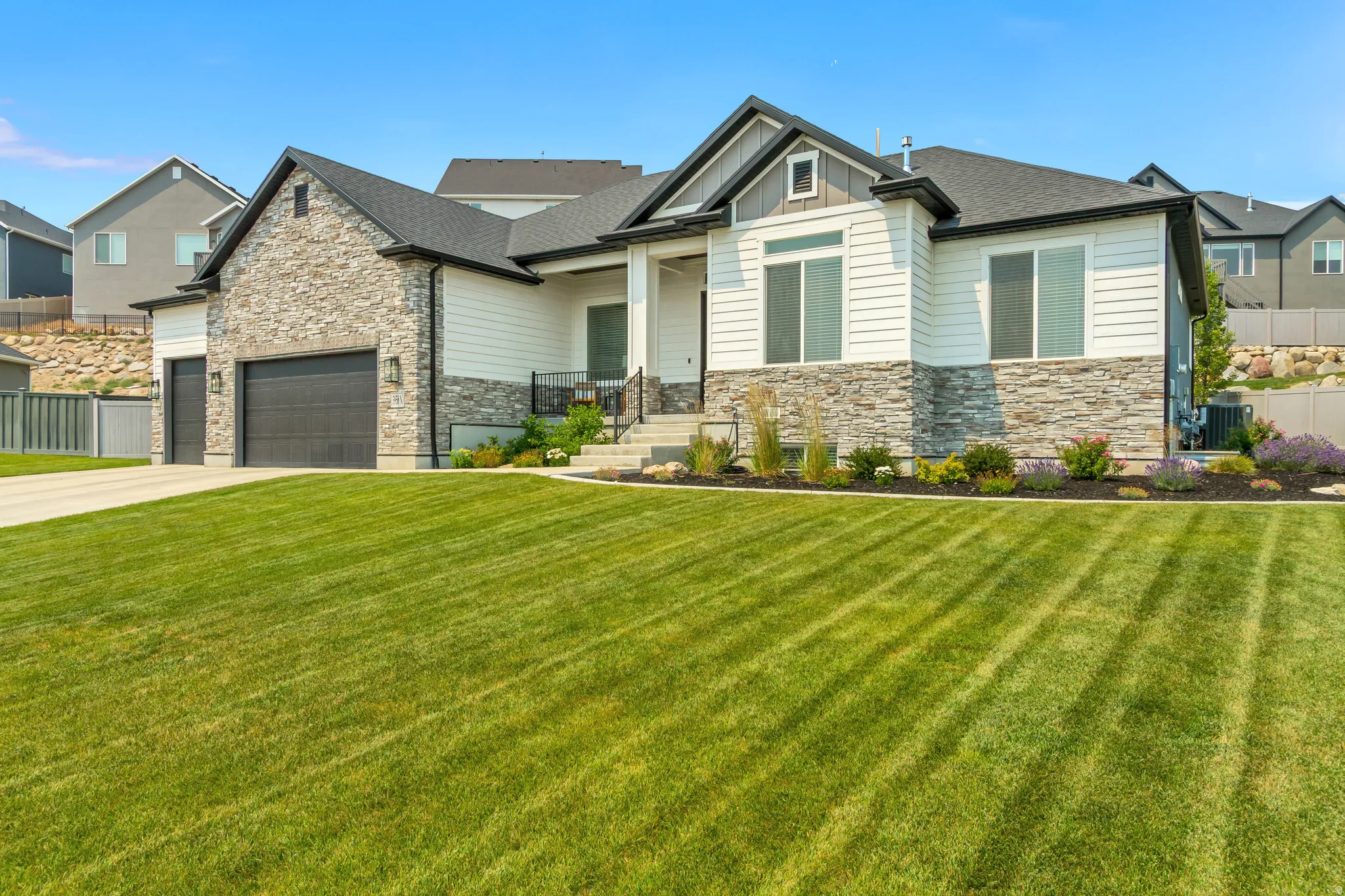 Contemporary single-story residence featuring a stone and siding exterior, a dark shingle roof, and a two-car garage with black doors