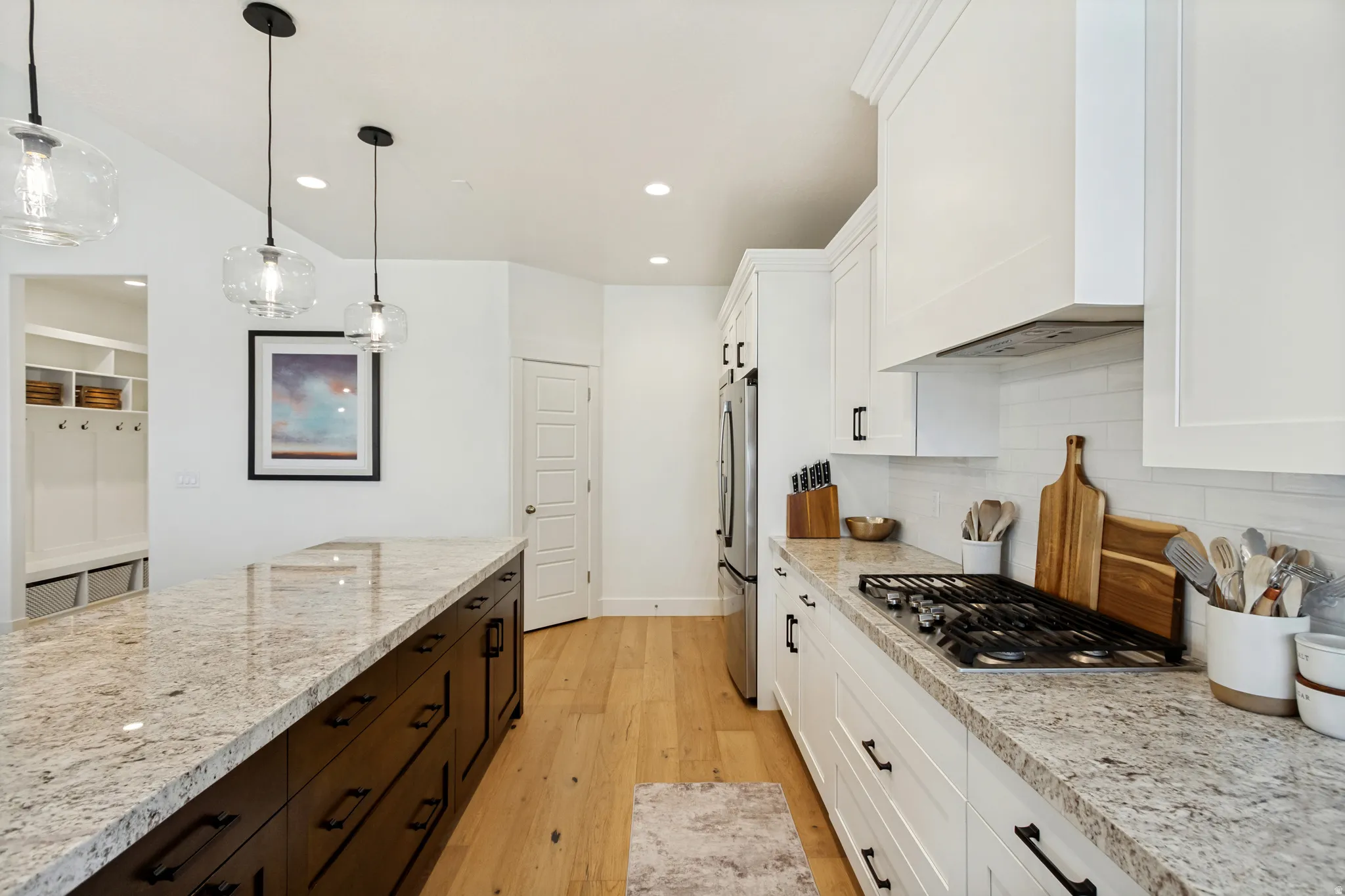Kitchen featuring a large central island with a light-toned countertop, a gas cooktop, white upper and lower cabinetry, and wood-finish flooring