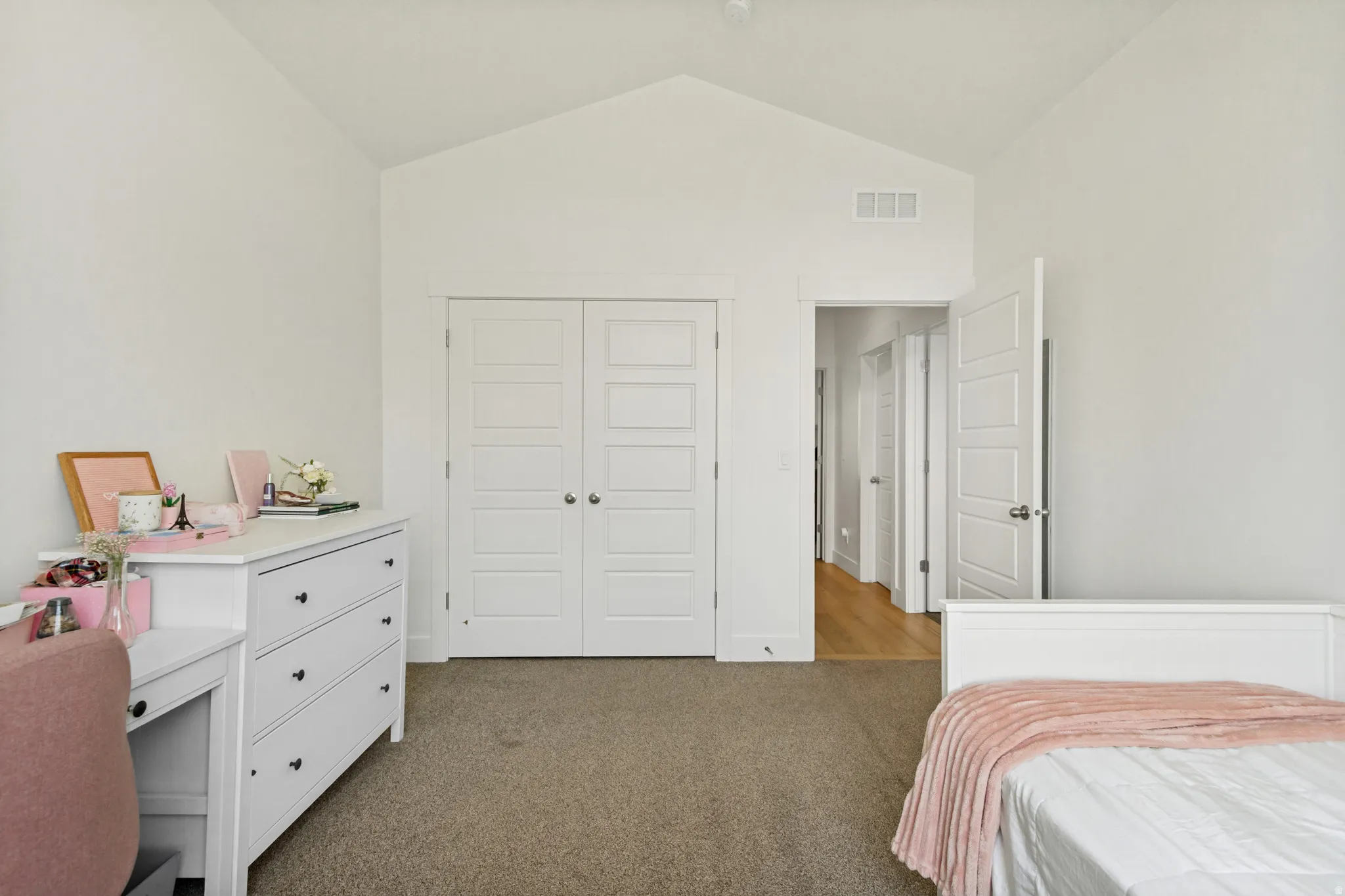 Vaulted ceiling with white walls, carpeted flooring, and a double-door closet with paneled doors