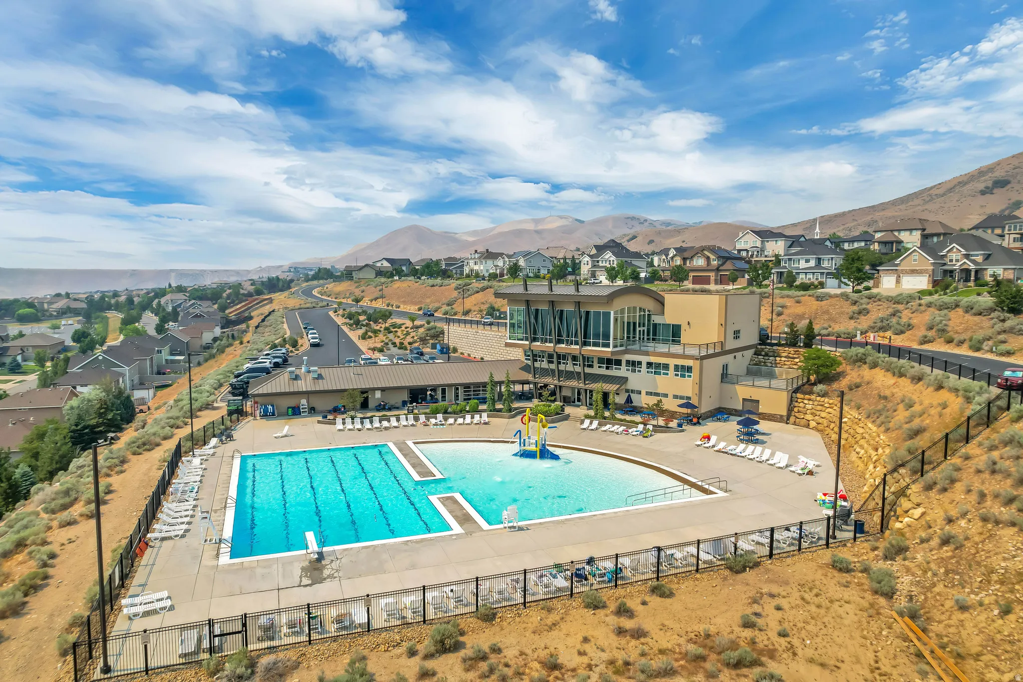Expansive community pool area featuring a multi-lane lap pool, a curved leisure pool with a water feature, and extensive surrounding decking