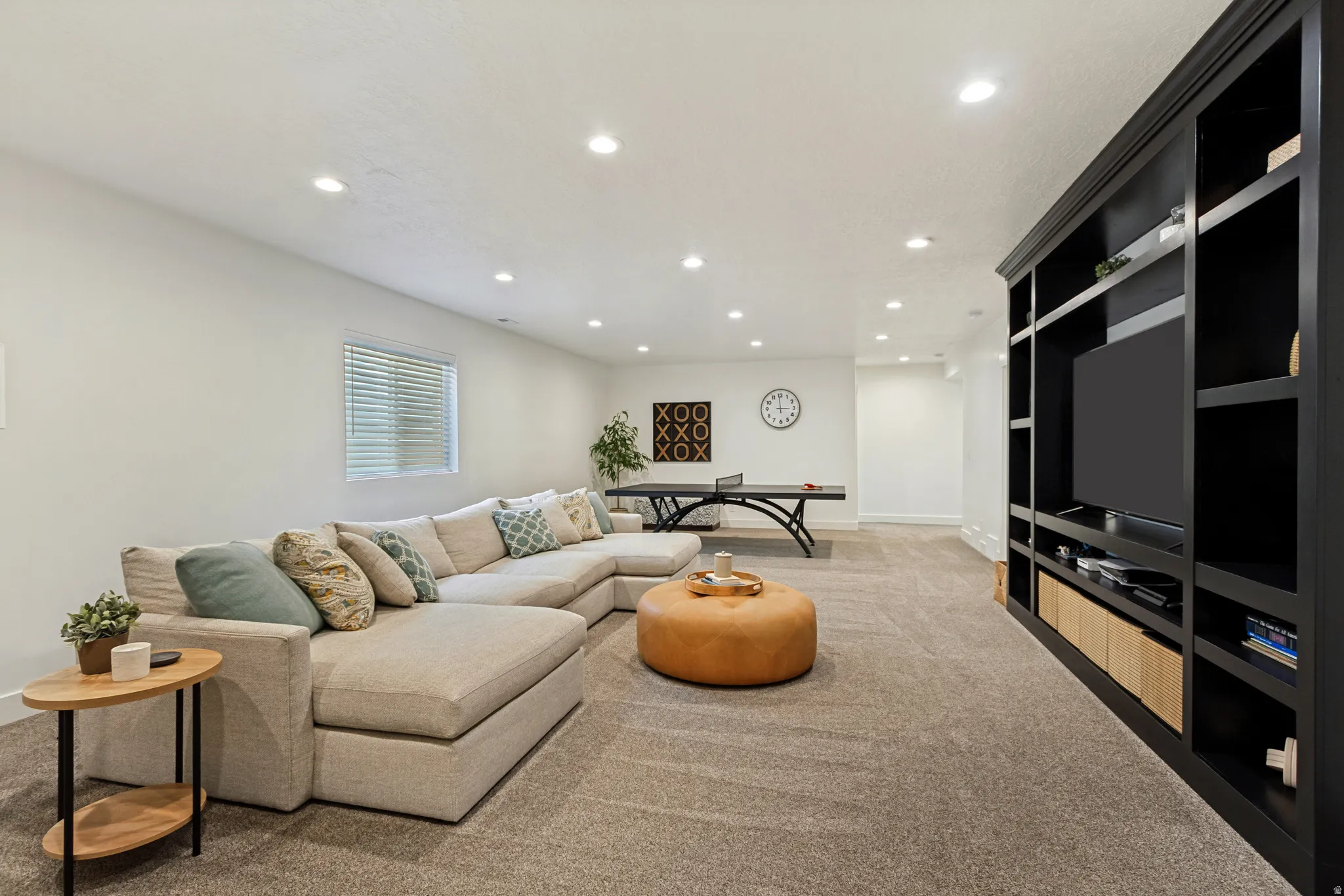 Spacious recreational room featuring a large built-in shelving unit, recessed lighting, and light-colored carpeting