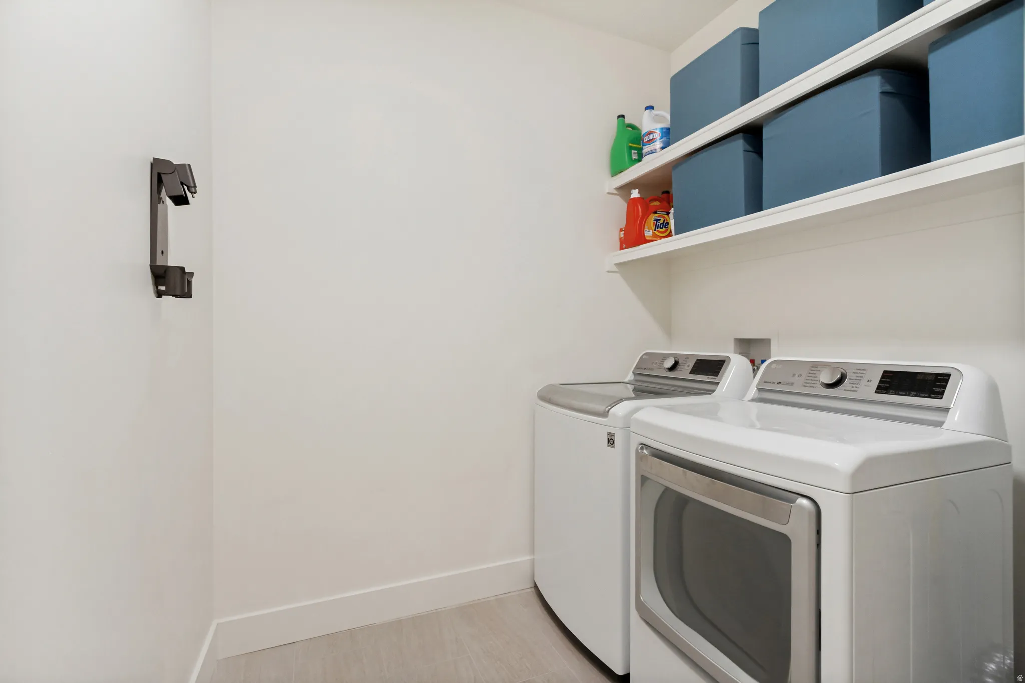 Dedicated laundry area featuring a washer and dryer, light-toned flooring, white walls, and built-in white shelving for storage