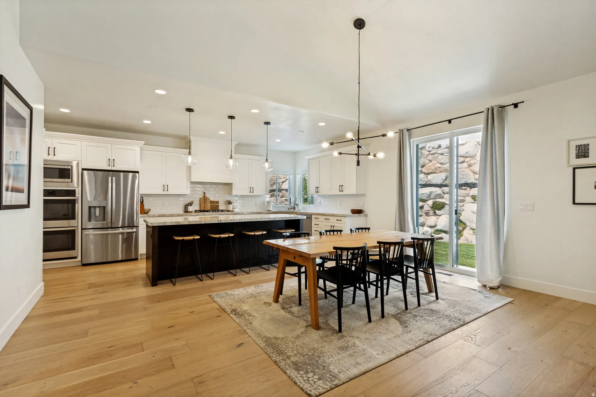 Spacious kitchen and dining area featuring light wood-finish flooring, white cabinetry, stainless steel appliances, a large island with dark wood-finish cabinetry, and a sliding glass door to the exterior