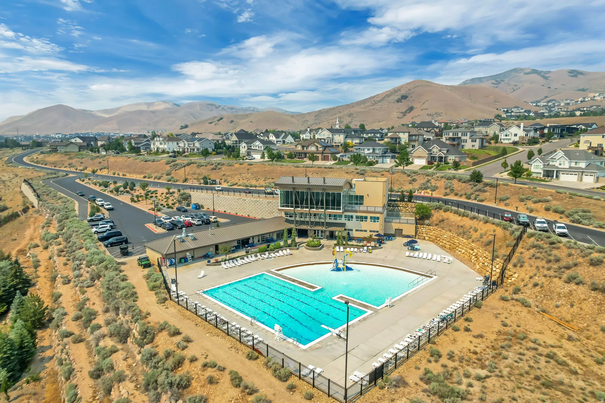 Community pool area featuring a large swimming pool, a separate shallow pool, and an adjacent multi-level clubhouse building