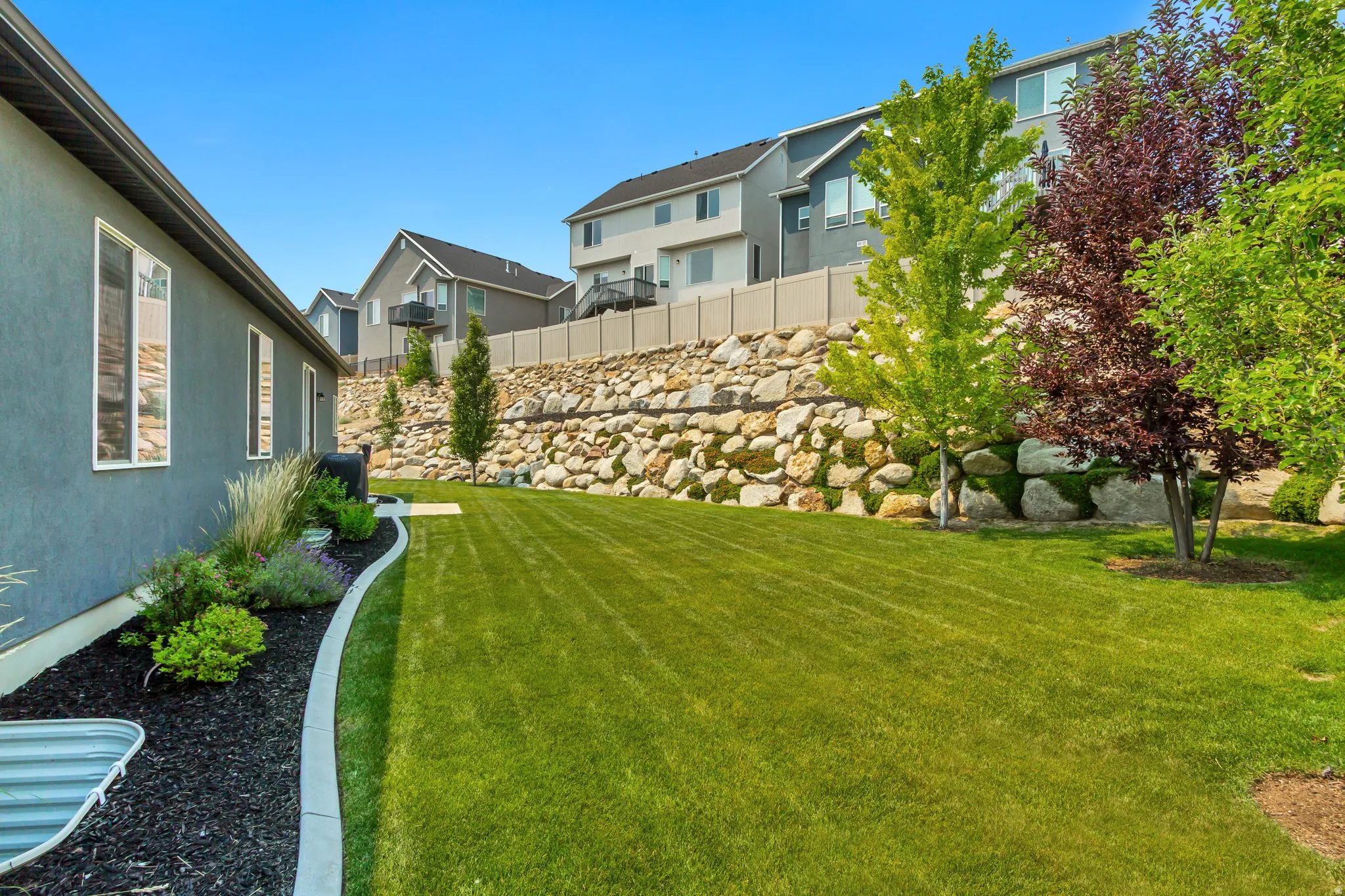 Expansive green lawn with a curved concrete border, an established rock retaining wall, and mature trees