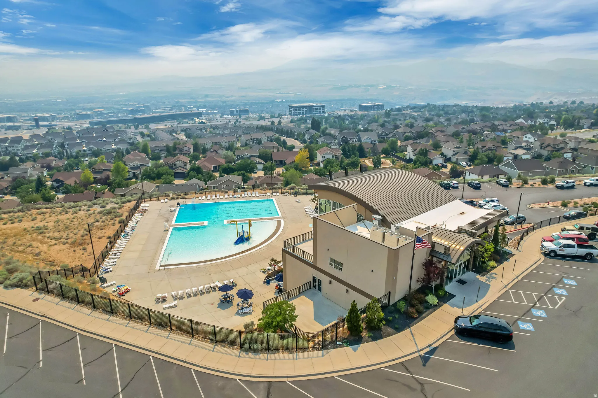 Community clubhouse with a curved metal roof, an expansive outdoor pool, and a surrounding paved deck