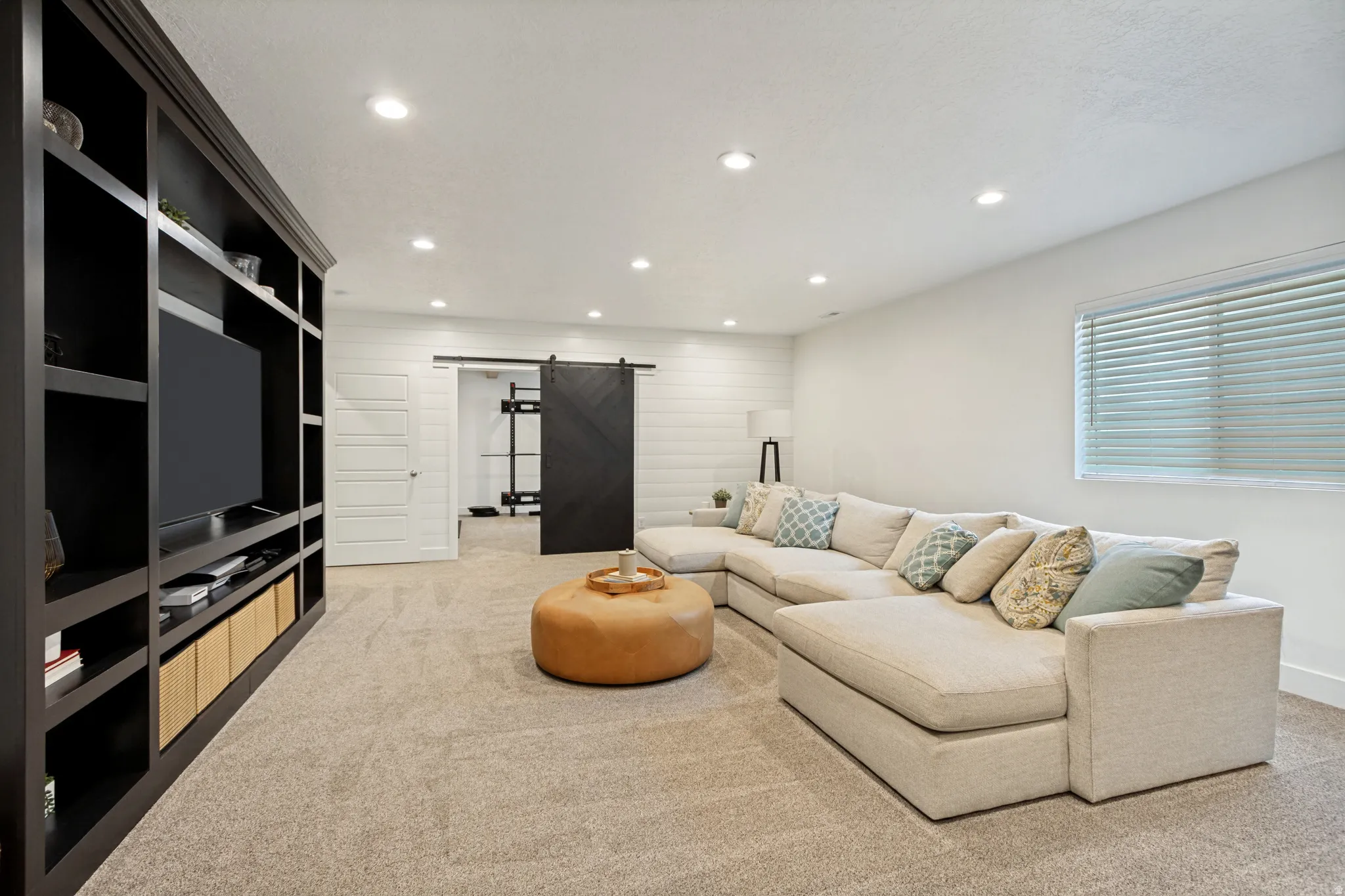 Built-in media center with dark wood finish, recessed lighting, carpet flooring, a white paneled accent wall, and a black barn door