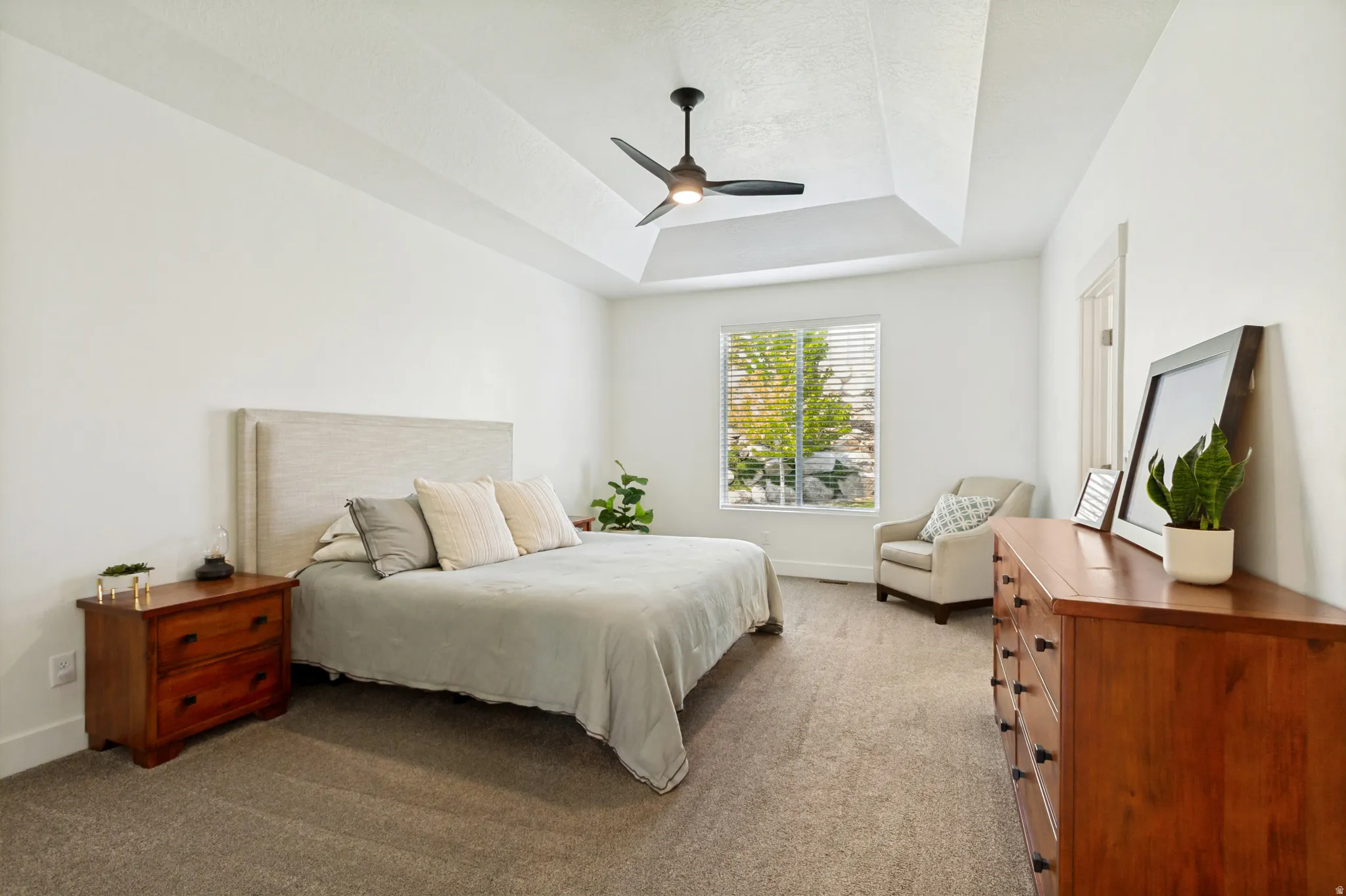 Spacious room featuring a tray ceiling, ceiling fan, carpet flooring, and window with blinds