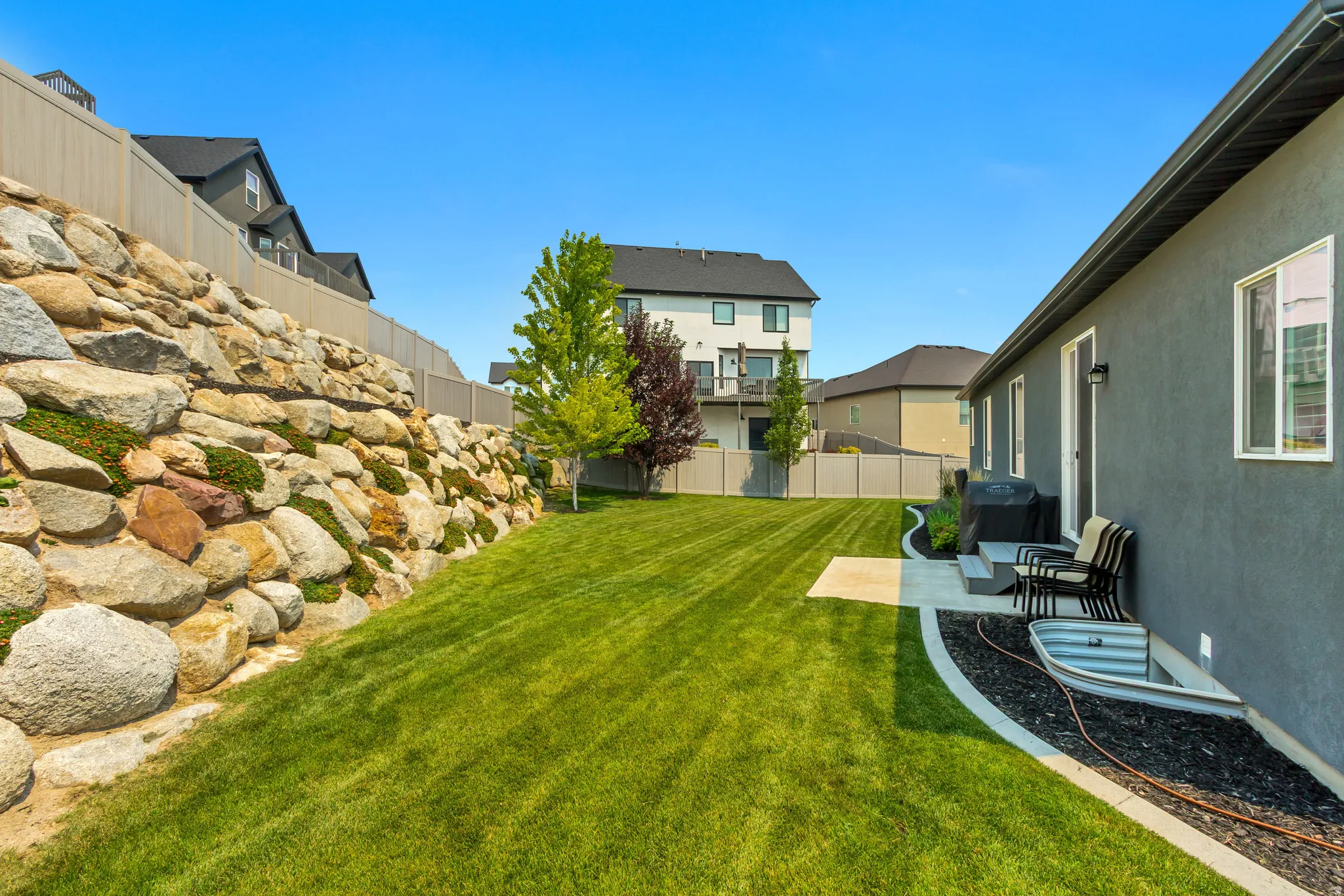 Expansive backyard featuring a rock retaining wall, vibrant green lawn, and a concrete patio