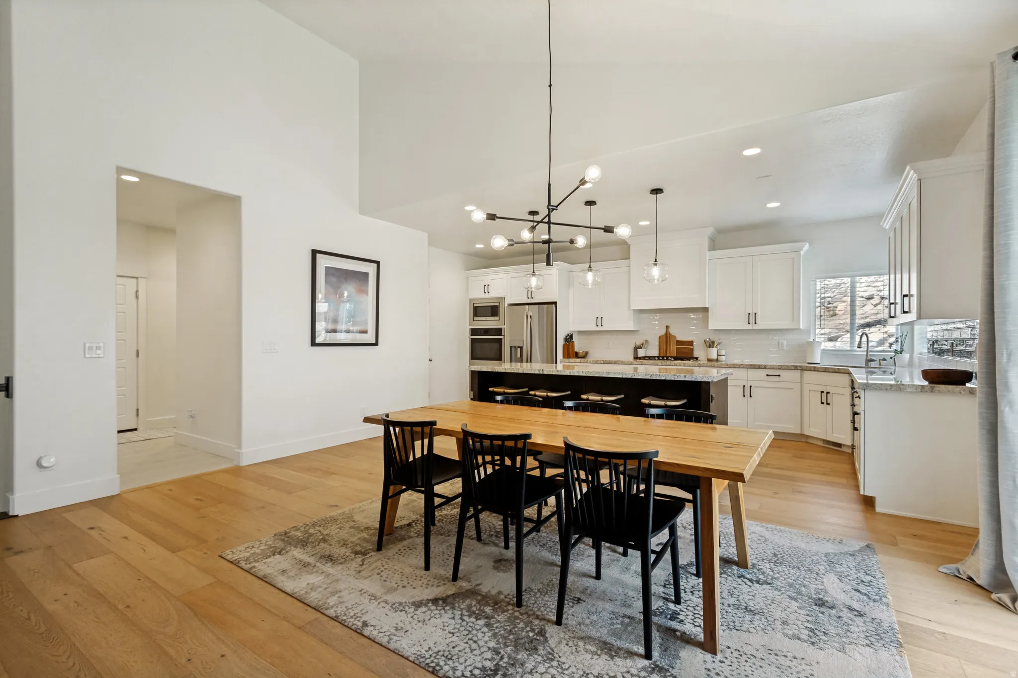 Open-concept living space featuring high ceilings, wood-finish flooring, a modern chandelier, a kitchen island with seating, and white cabinetry
