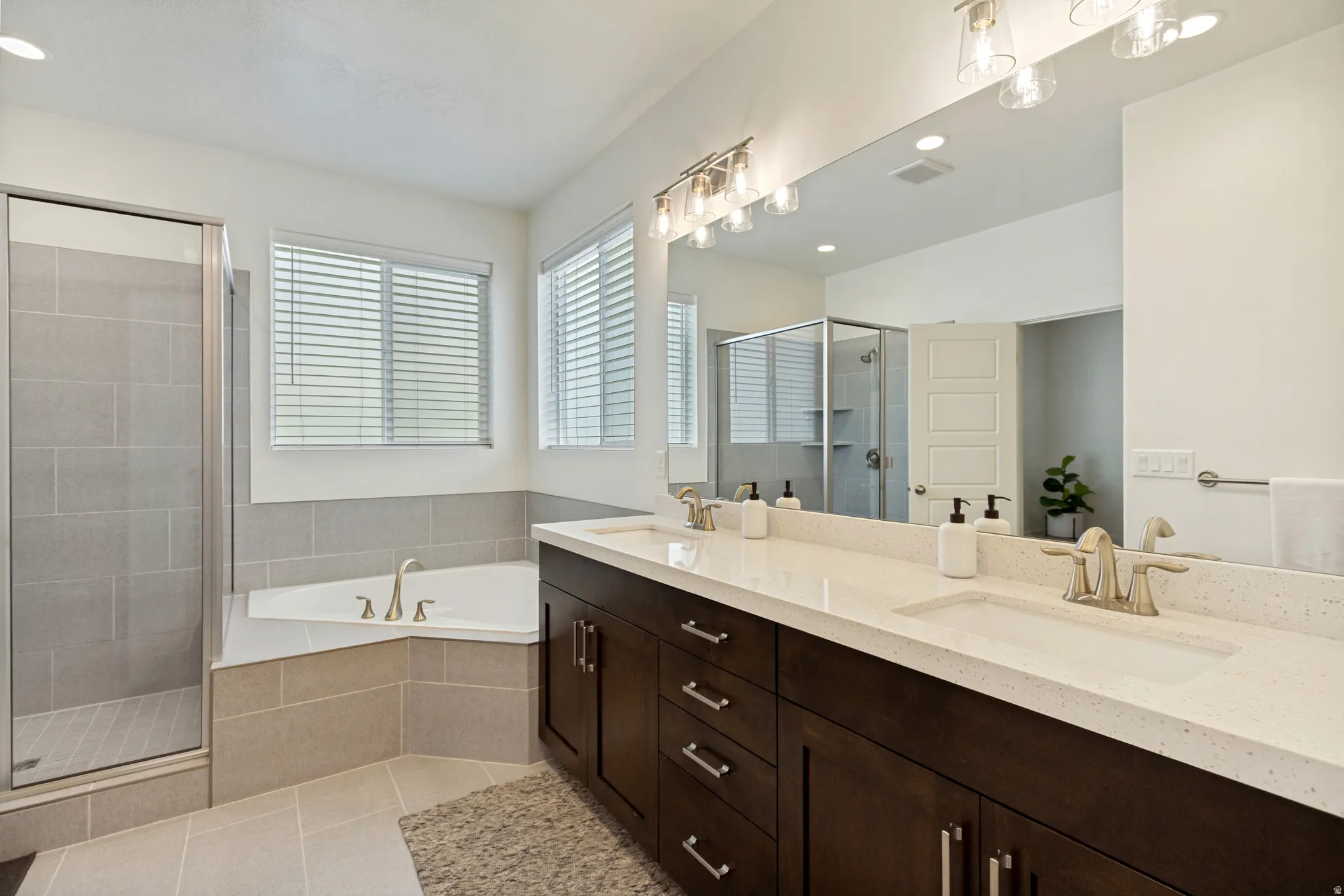 Bathroom featuring a dual vanity with a light-toned countertop, a corner soaking tub, a separate glass-enclosed shower, and tile flooring